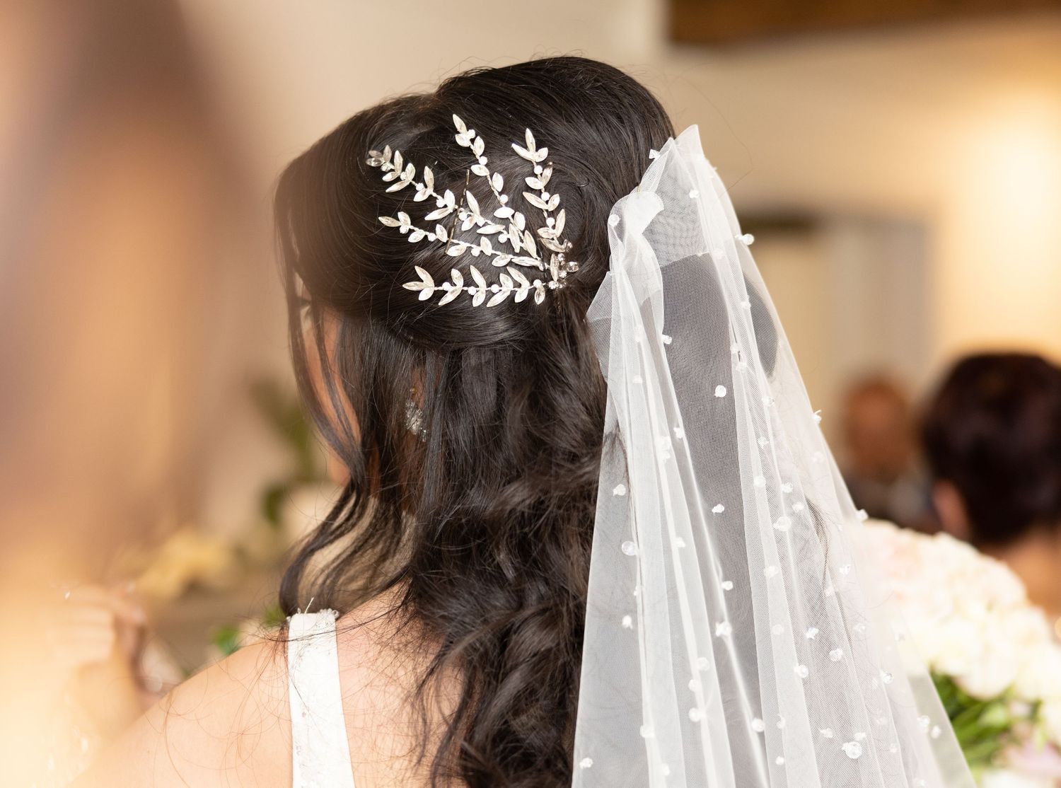 A bride wearing an elegant lace veil and floral hairpiece stands with dark wavy hair styled for her wedding day.