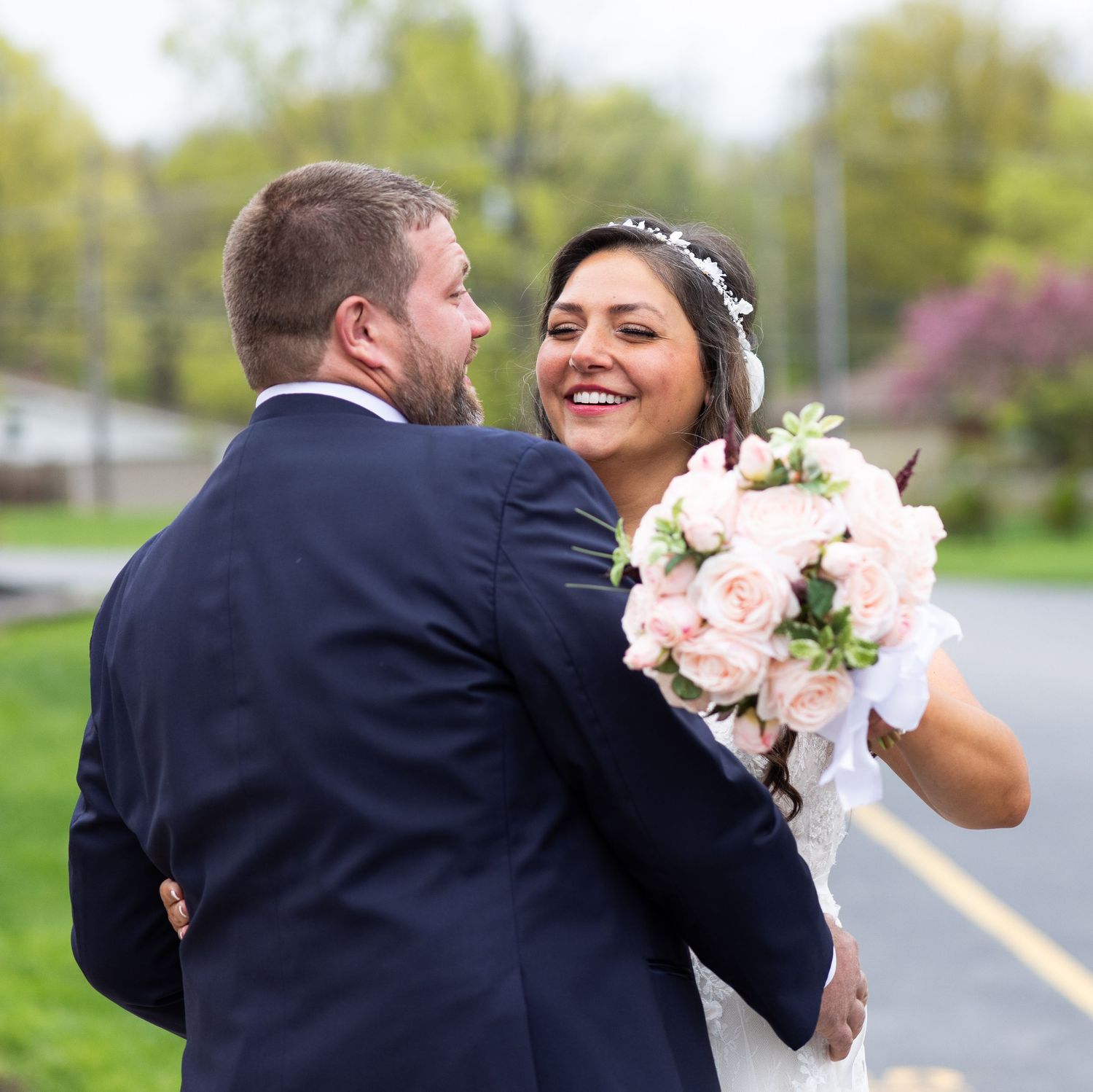 A couple in wedding attire share a romantic dip pose outdoors in a garden setting.