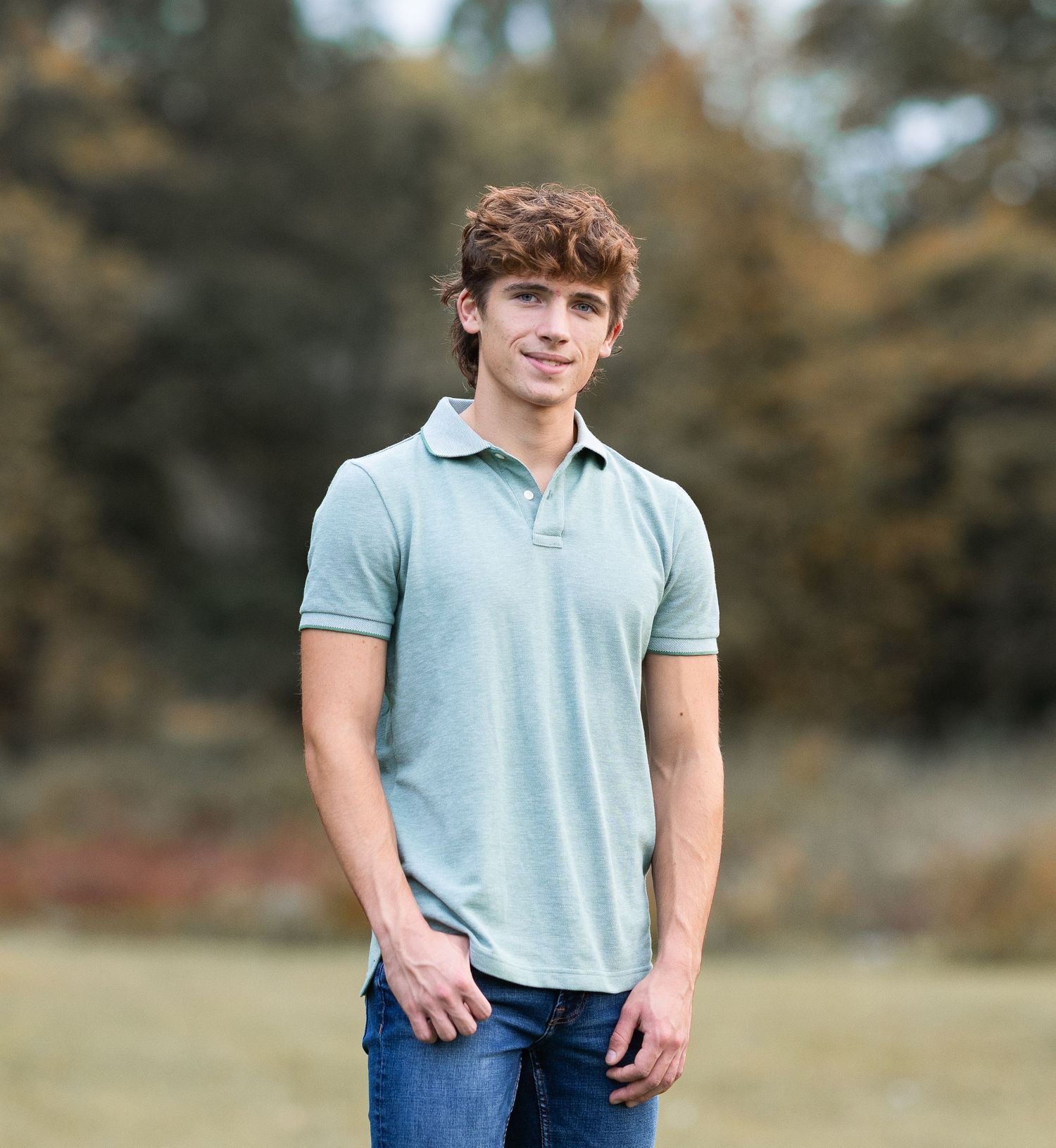 Young person in light blue polo shirt poses casually outdoors during a portrait session.
