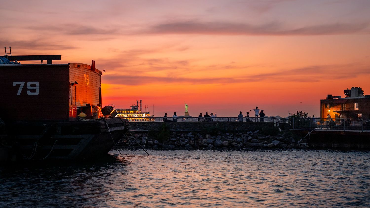 An orange sunset over the water in Red Hook, Brooklyn, with the Statue of Liberty in the distance.