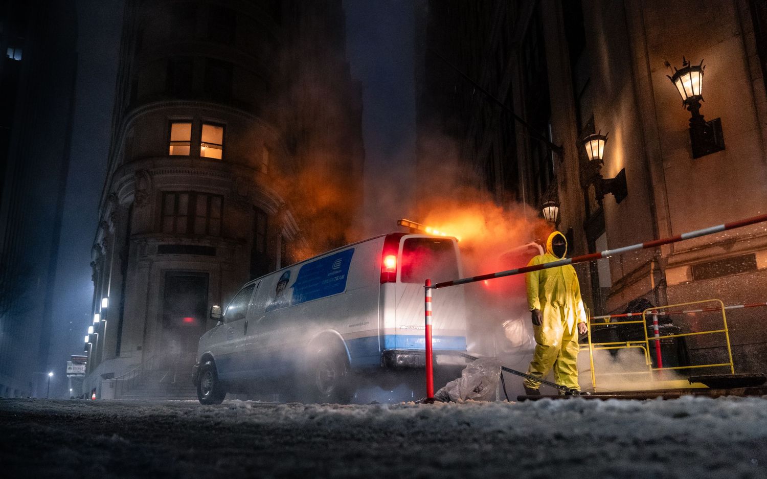 A city worker standing beside a steaming vehicle on a snow-covered New York City street at night.