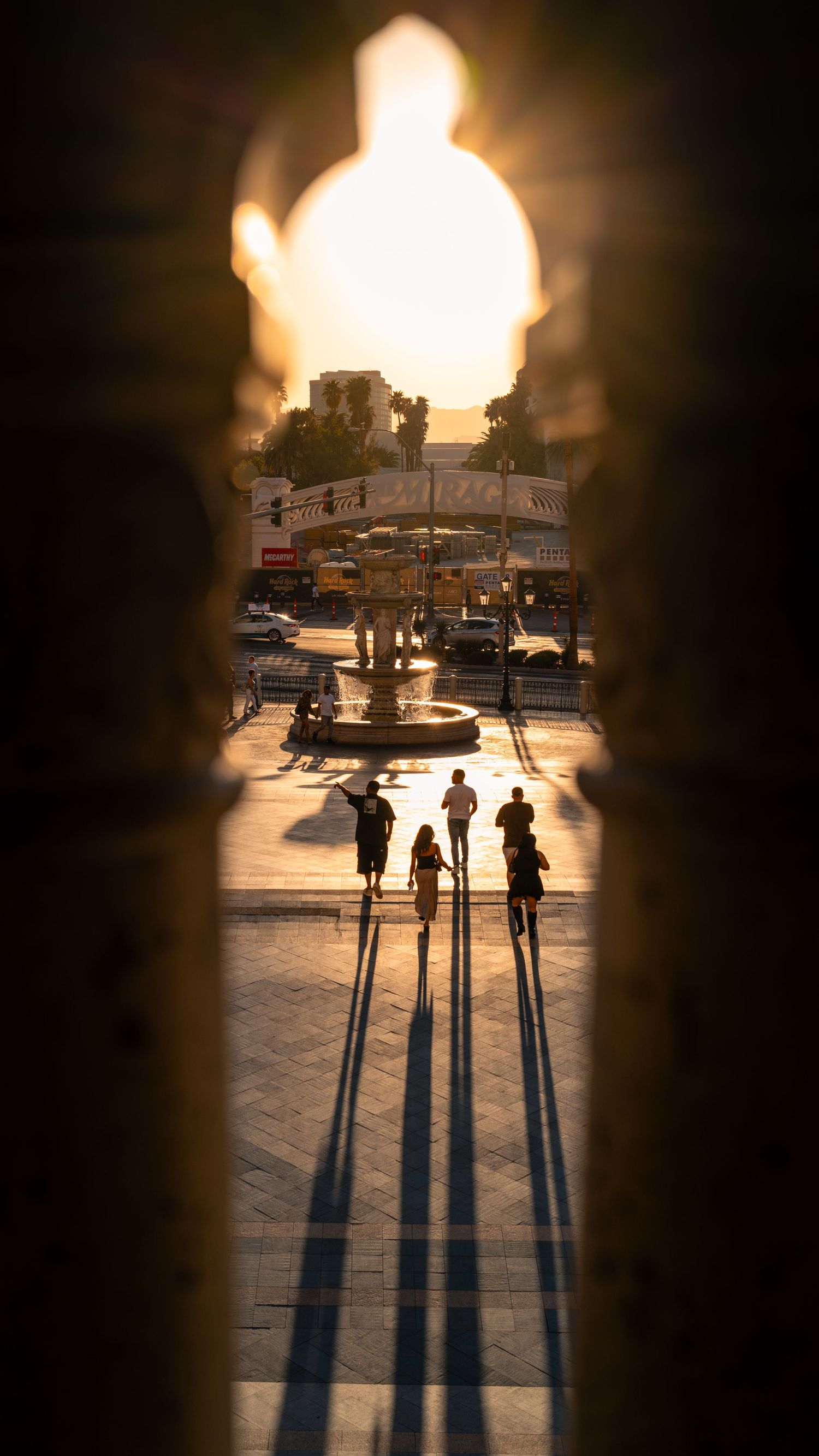 Long shadows of a group of friends stretching across the ground, framed by an arch in Las Vegas.