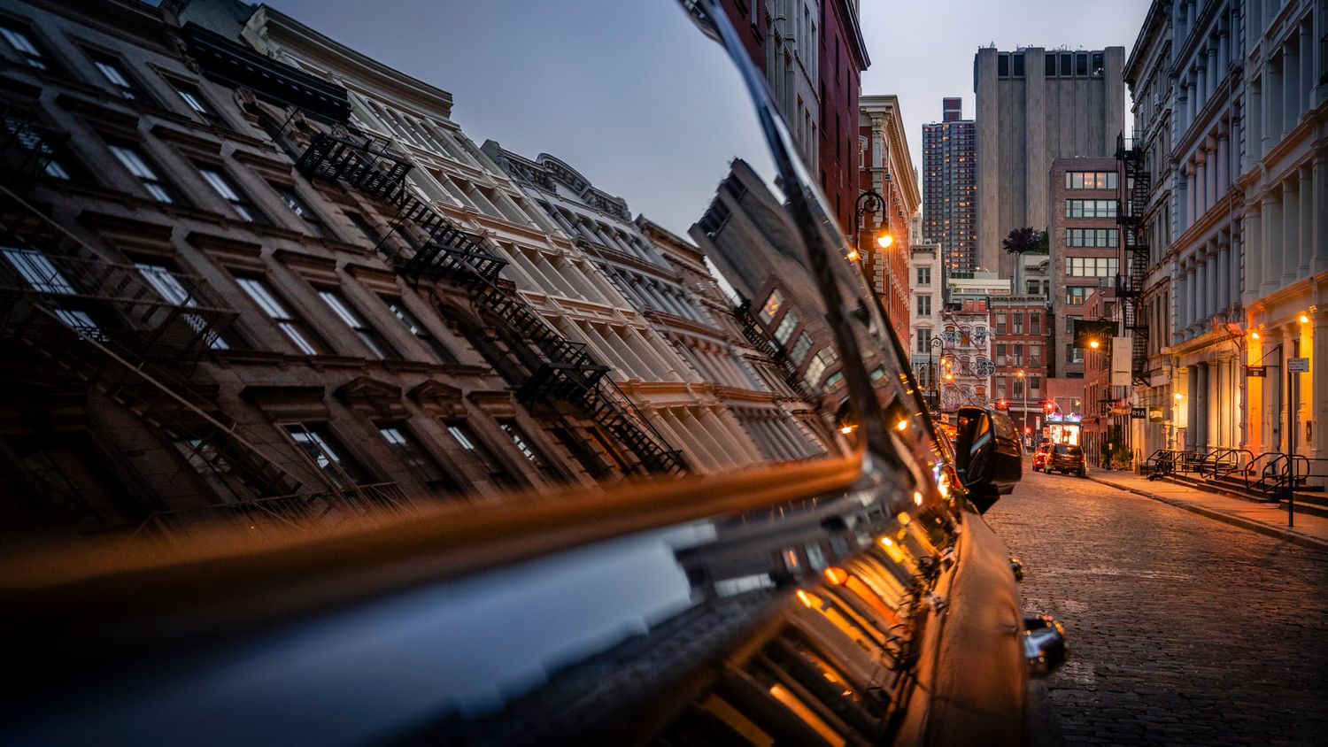 SoHo buildings reflected and distorted across the window of a parked car at dusk