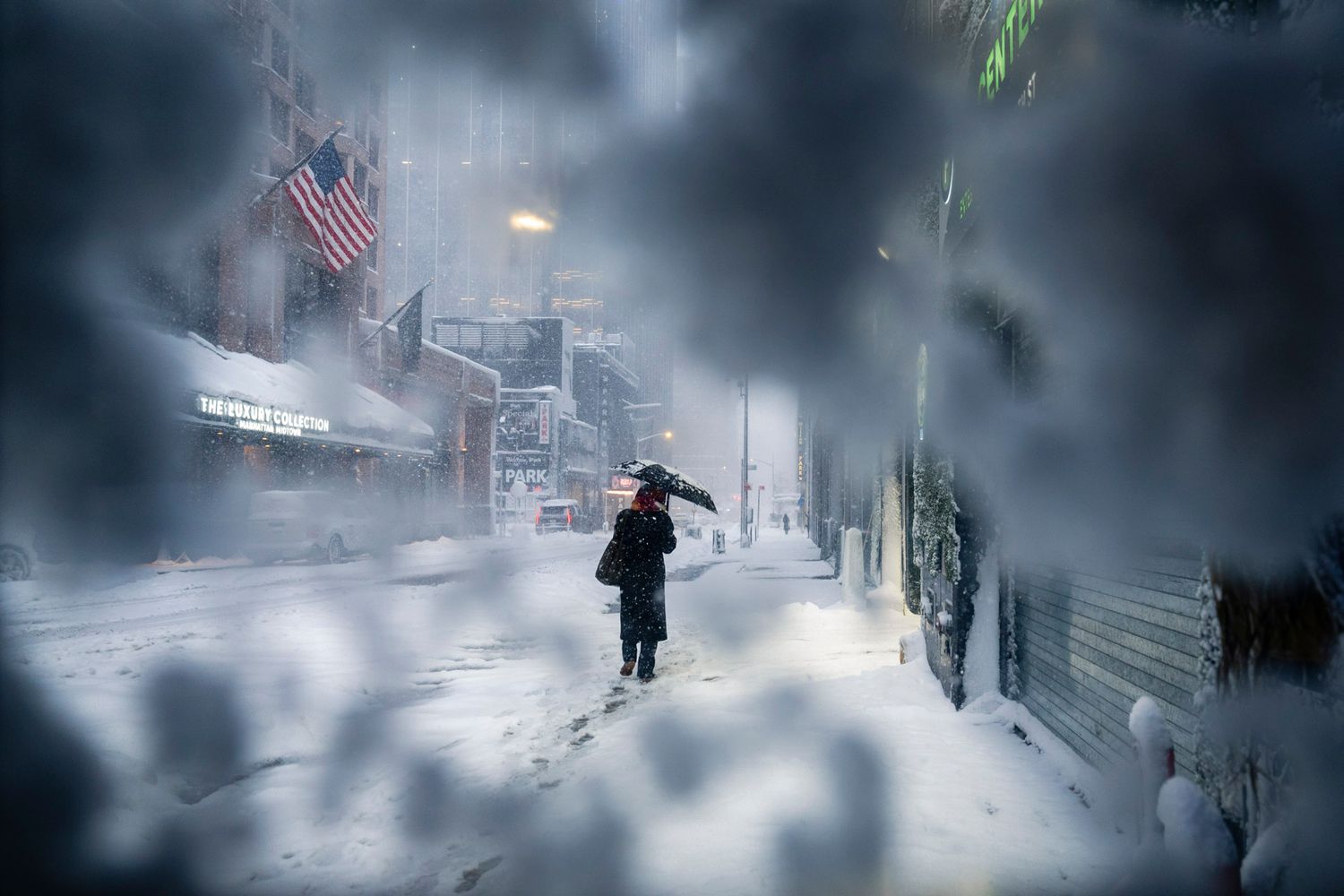Figure with an umbrella walking through a New York City snowstorm seen through a frost-covered window