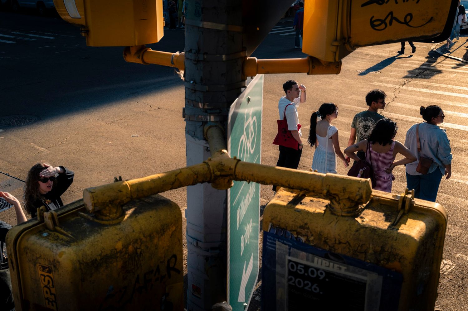 Pedestrians squinting in warm sunlight framed by yellow traffic lights at an intersection
