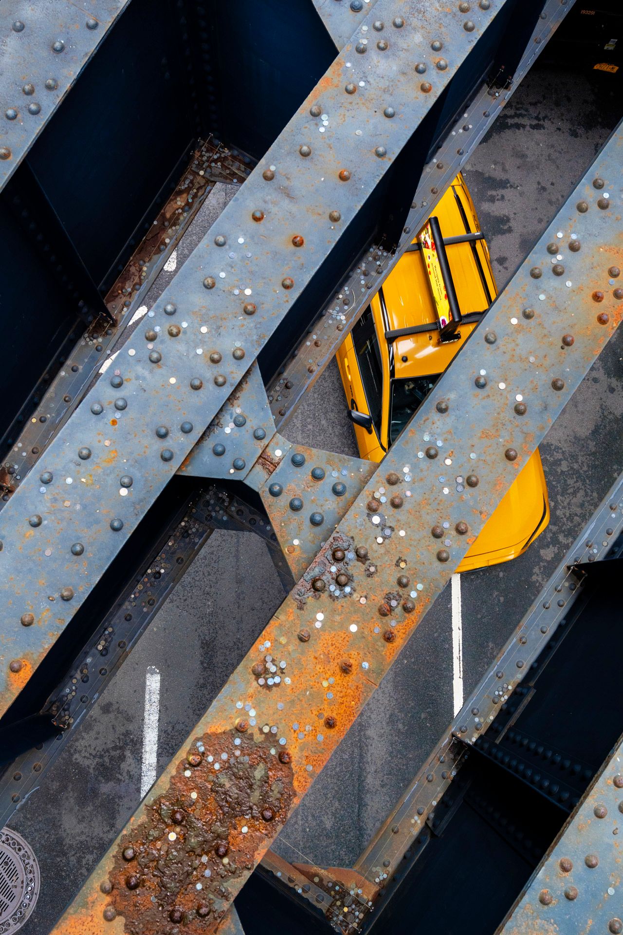 Yellow taxi framed between intersecting steel beams of a New York City bridge