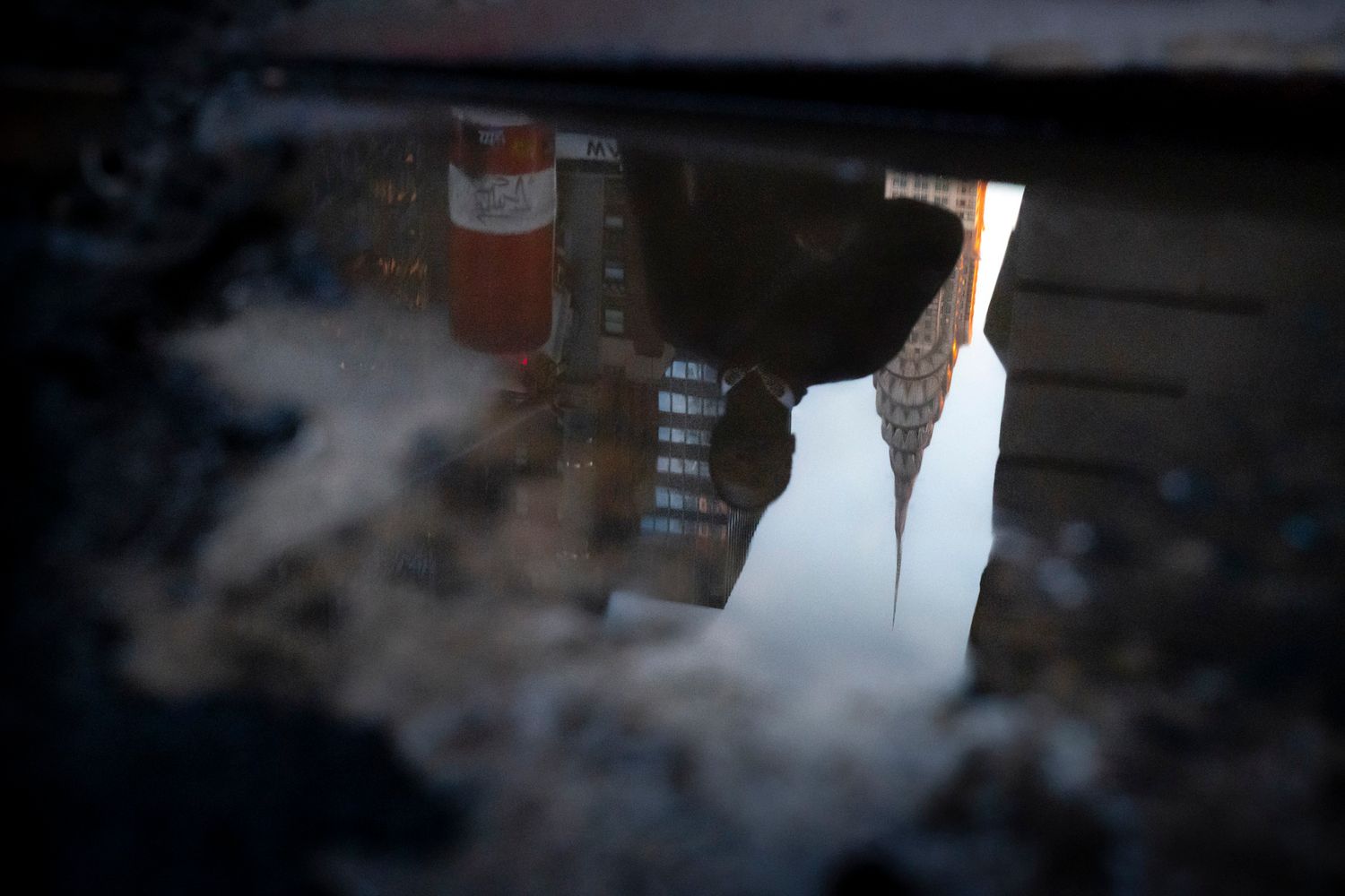 Reflection of the Chrysler Building and a pedestrian in a street puddle