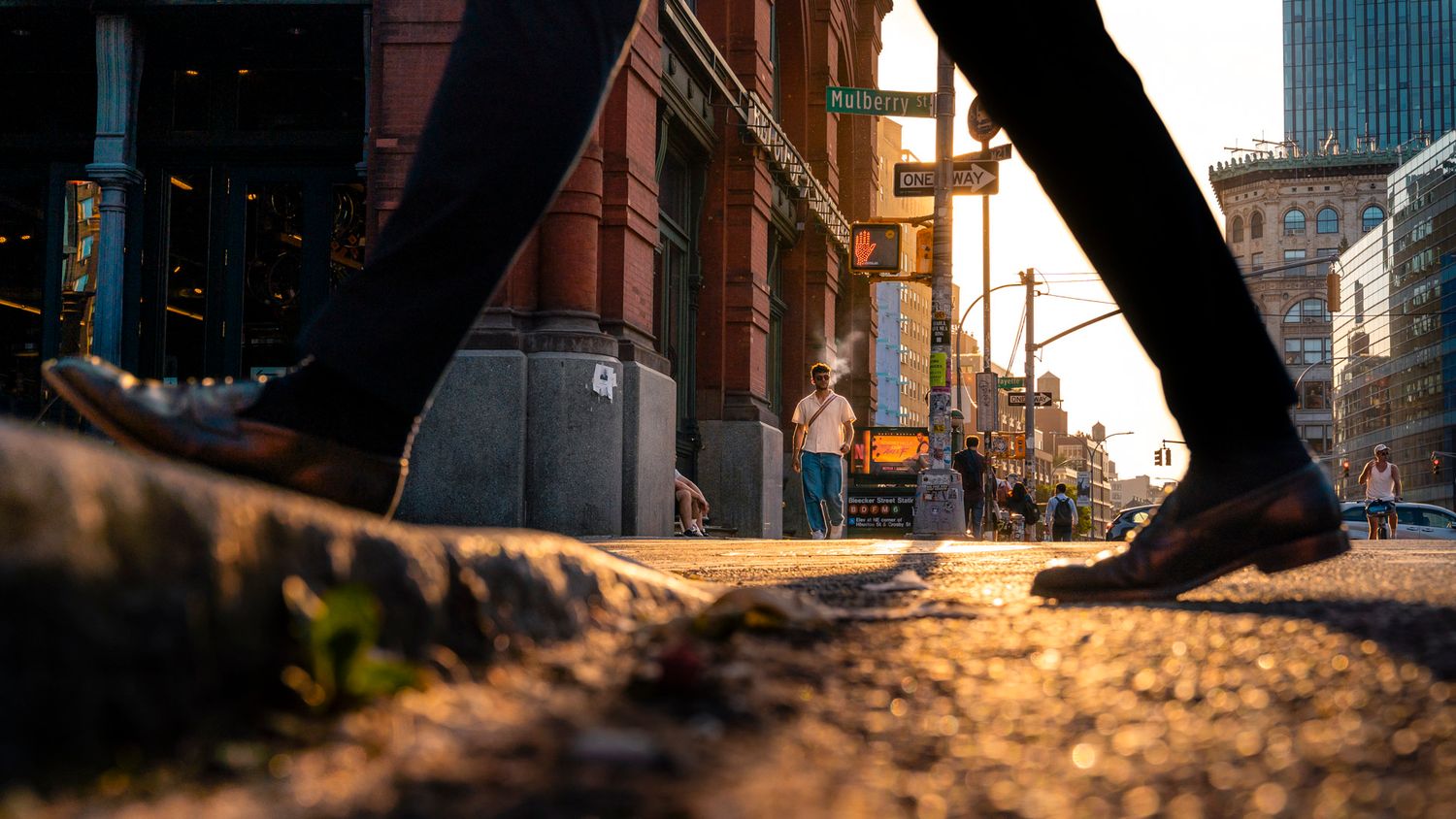 Pedestrian smoking and crossing a New York City street framed between passing legs in golden evening light