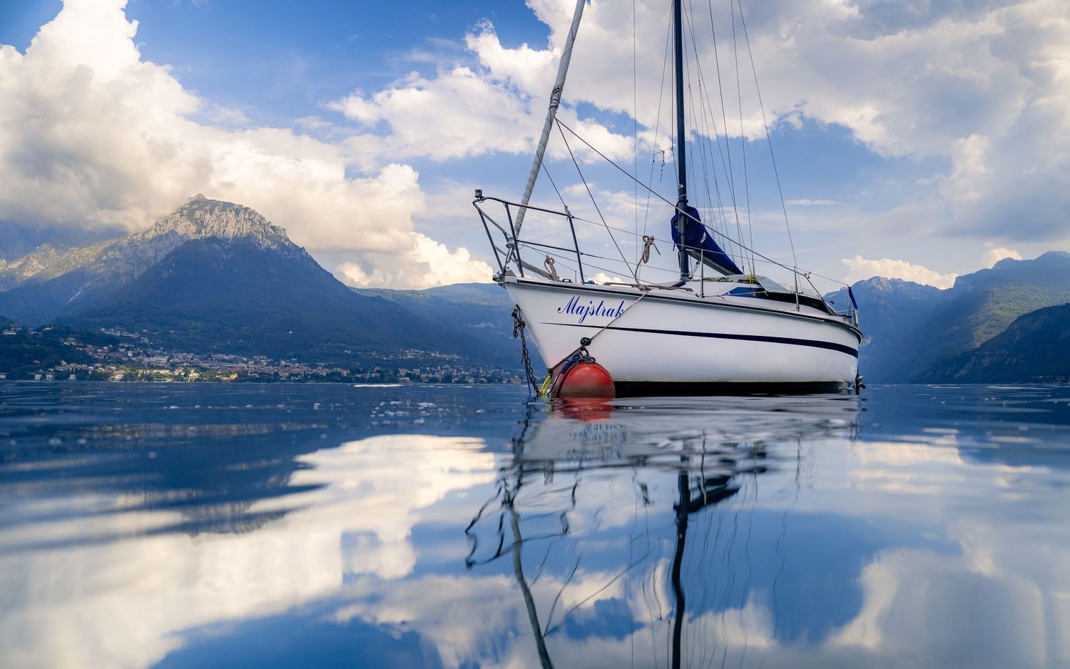 A sailboat resting on calm water in Lake Como, Italy, reflected against mountains and a wide blue sky.
