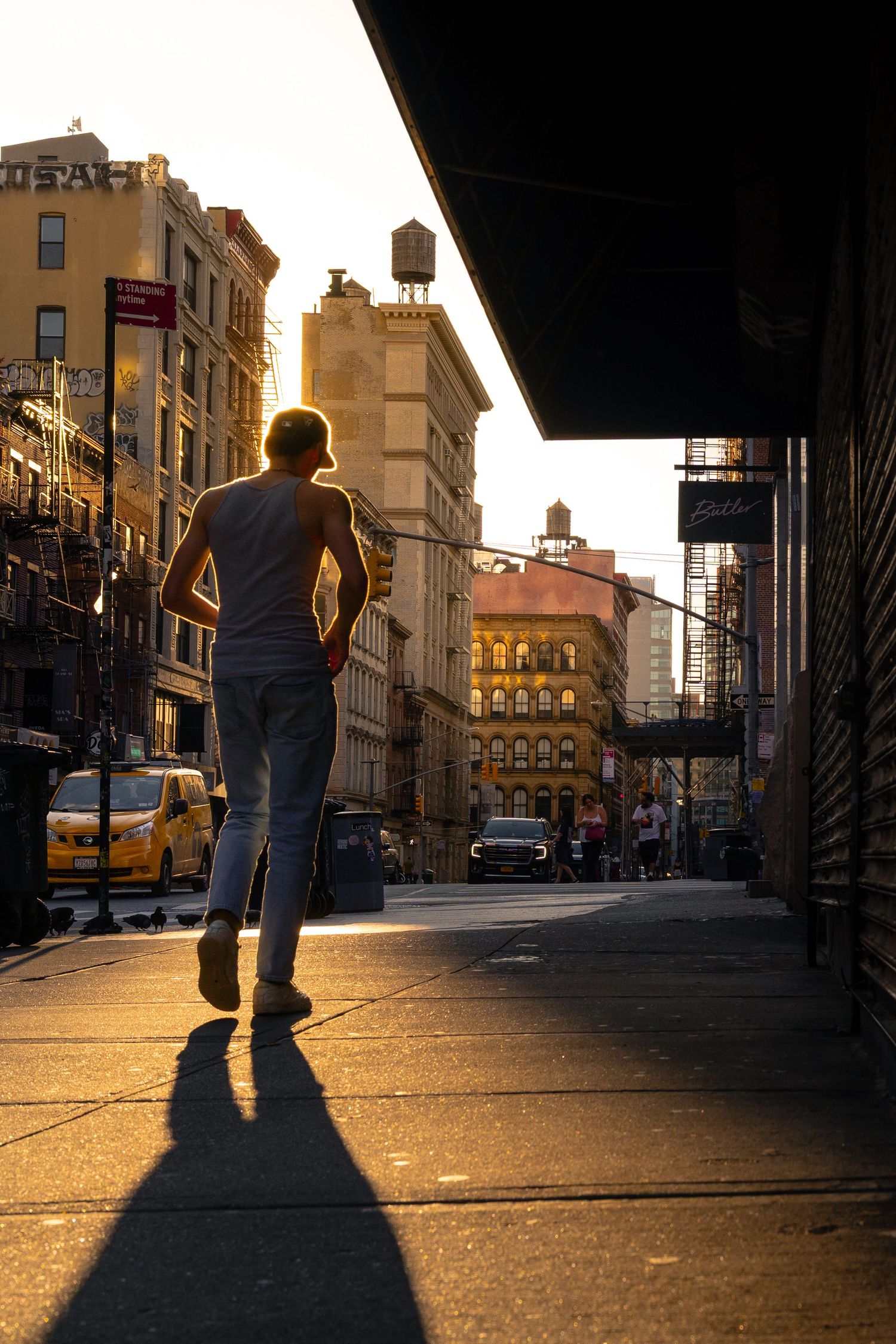Silhouette of a man walking through SoHo as golden light falls between buildings and a rooftop water tower.