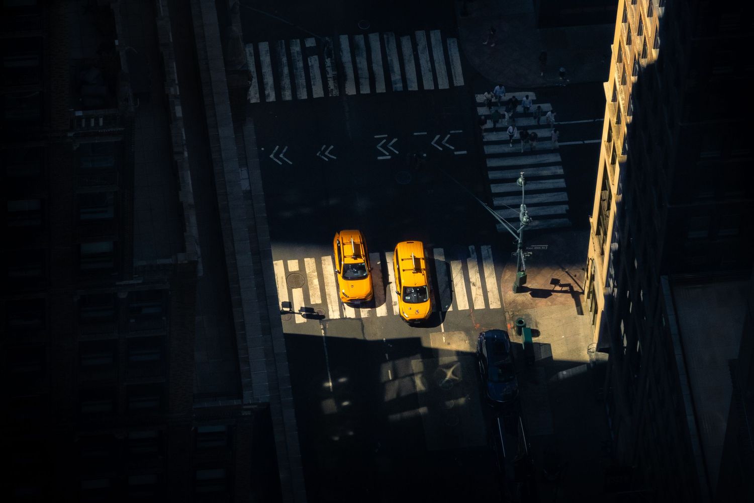 Two taxis illuminated by sun beaming through shadows cast by skyscrapers in Midtown New York.