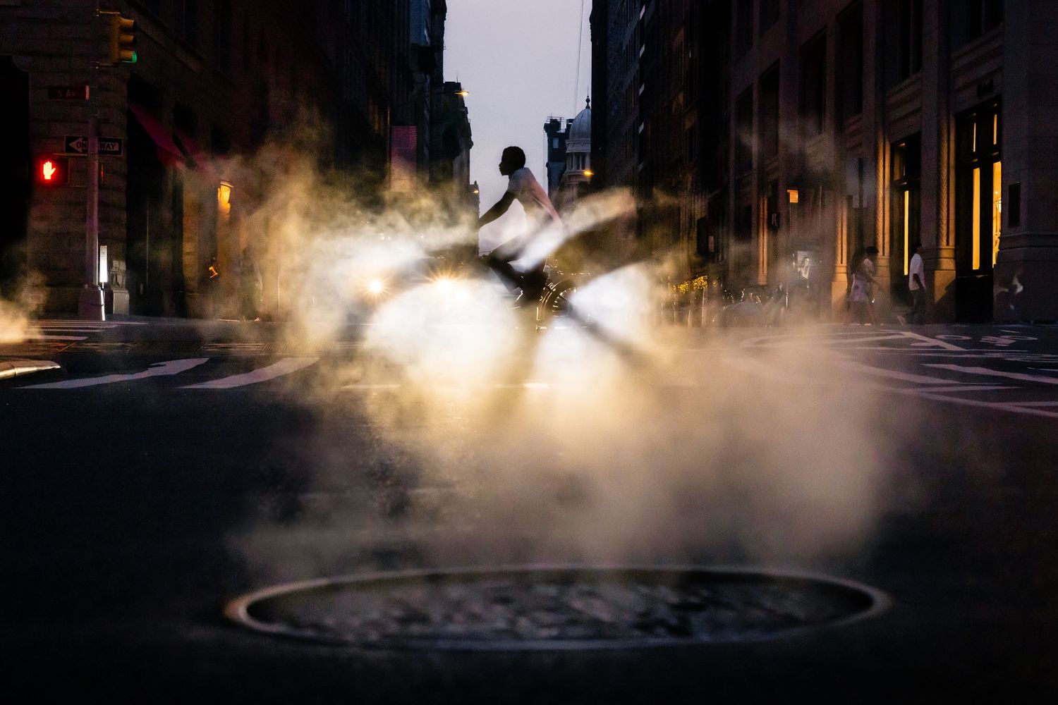 Cyclist silhouetted against street steam rising from a manhole in New York City.