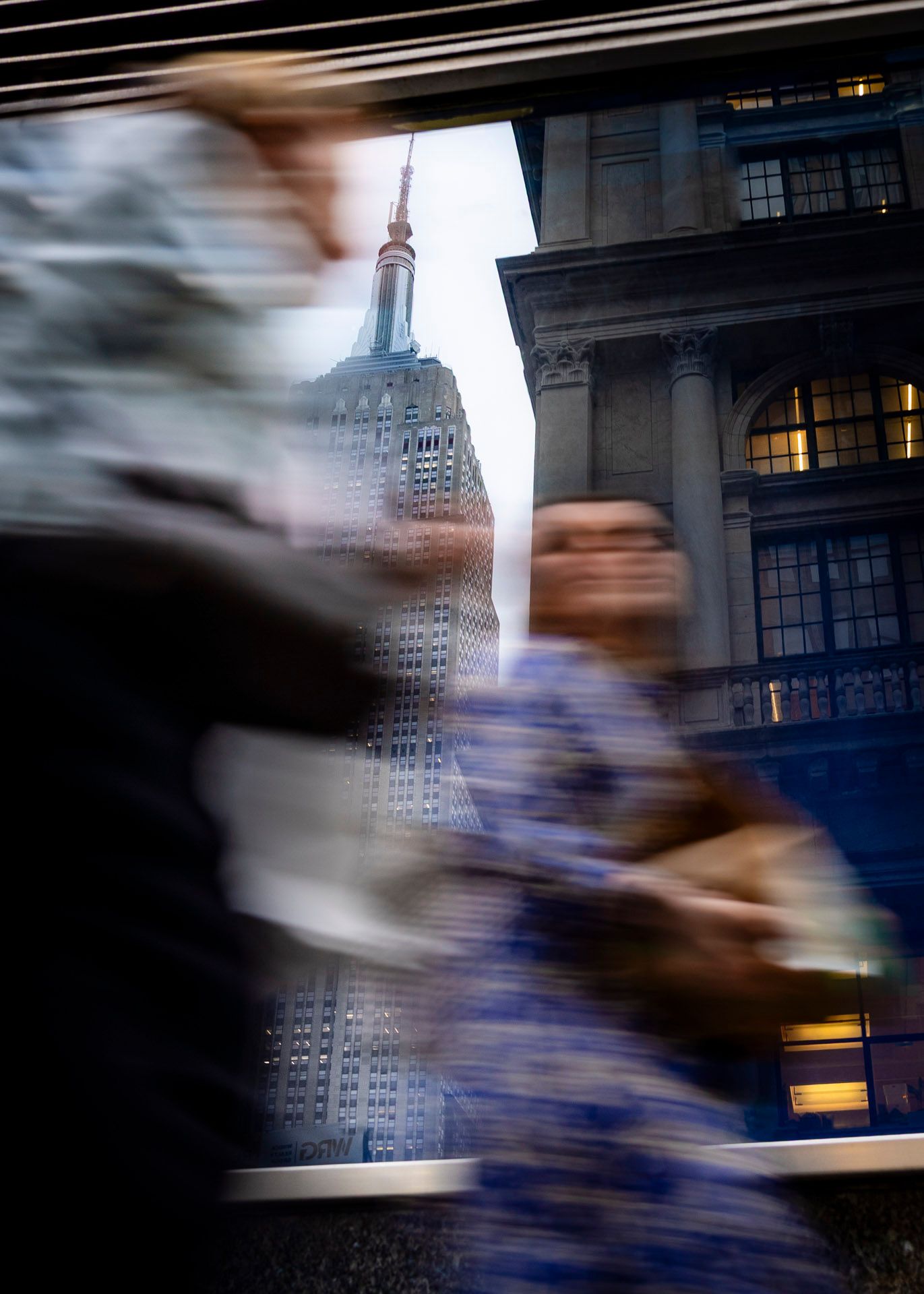 Blurred pedestrians passing the Empire State Building reflected in a window