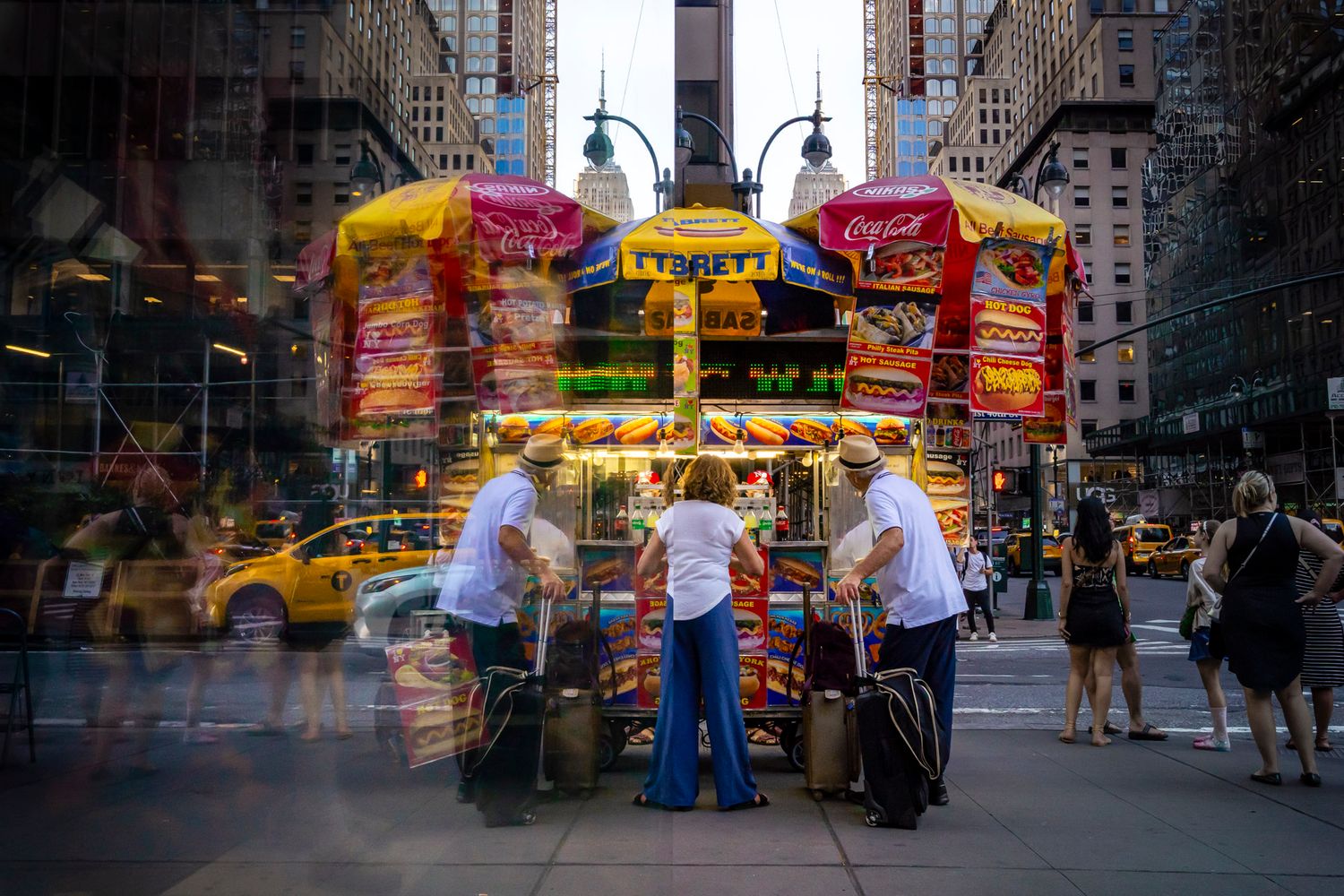 Hot dog cart and tourists mirrored symmetrically through reflections in Midtown Manhattan
