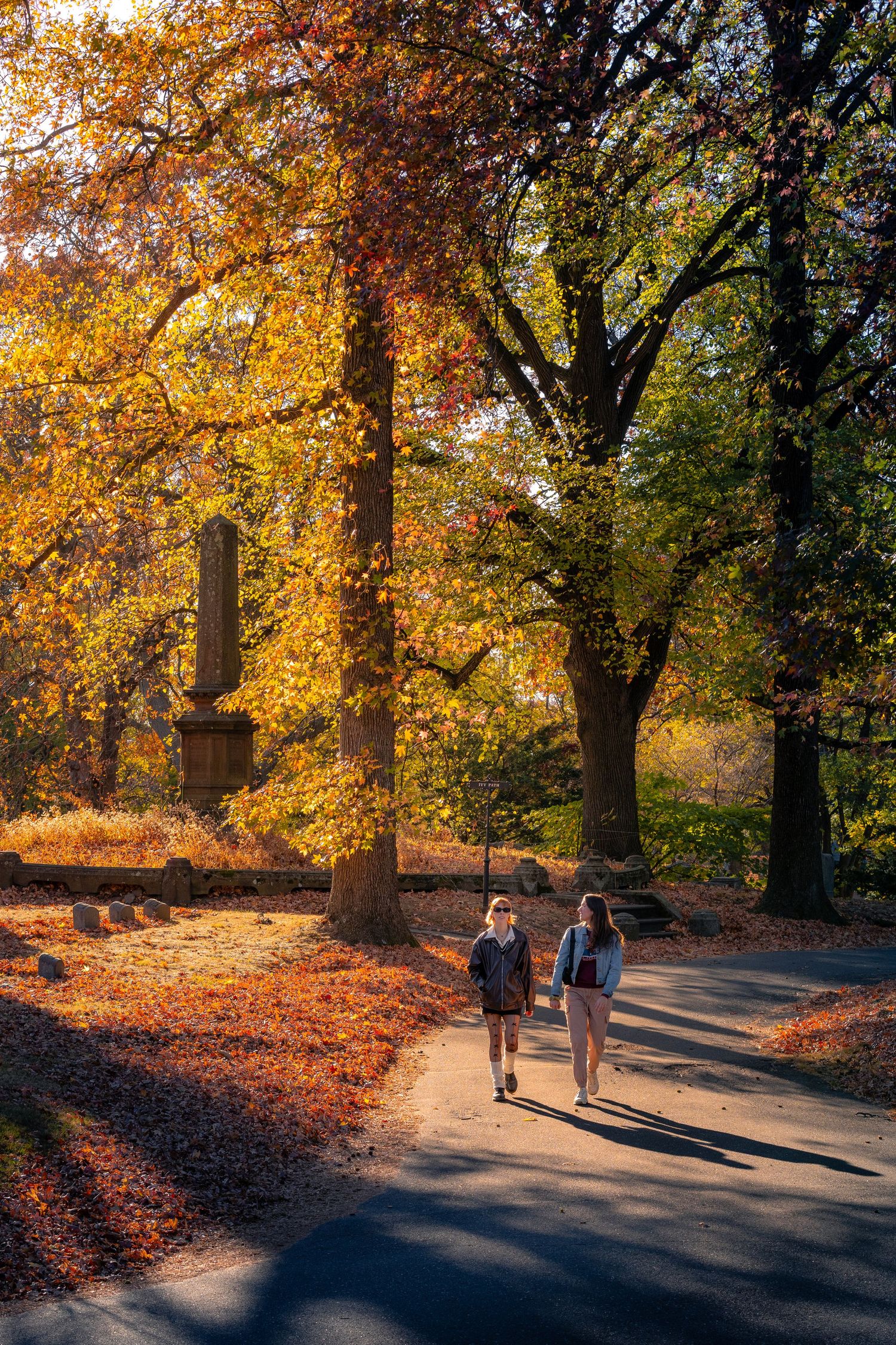 Two people walking along a path in Green-Wood Cemetery surrounded by autumn foliage.