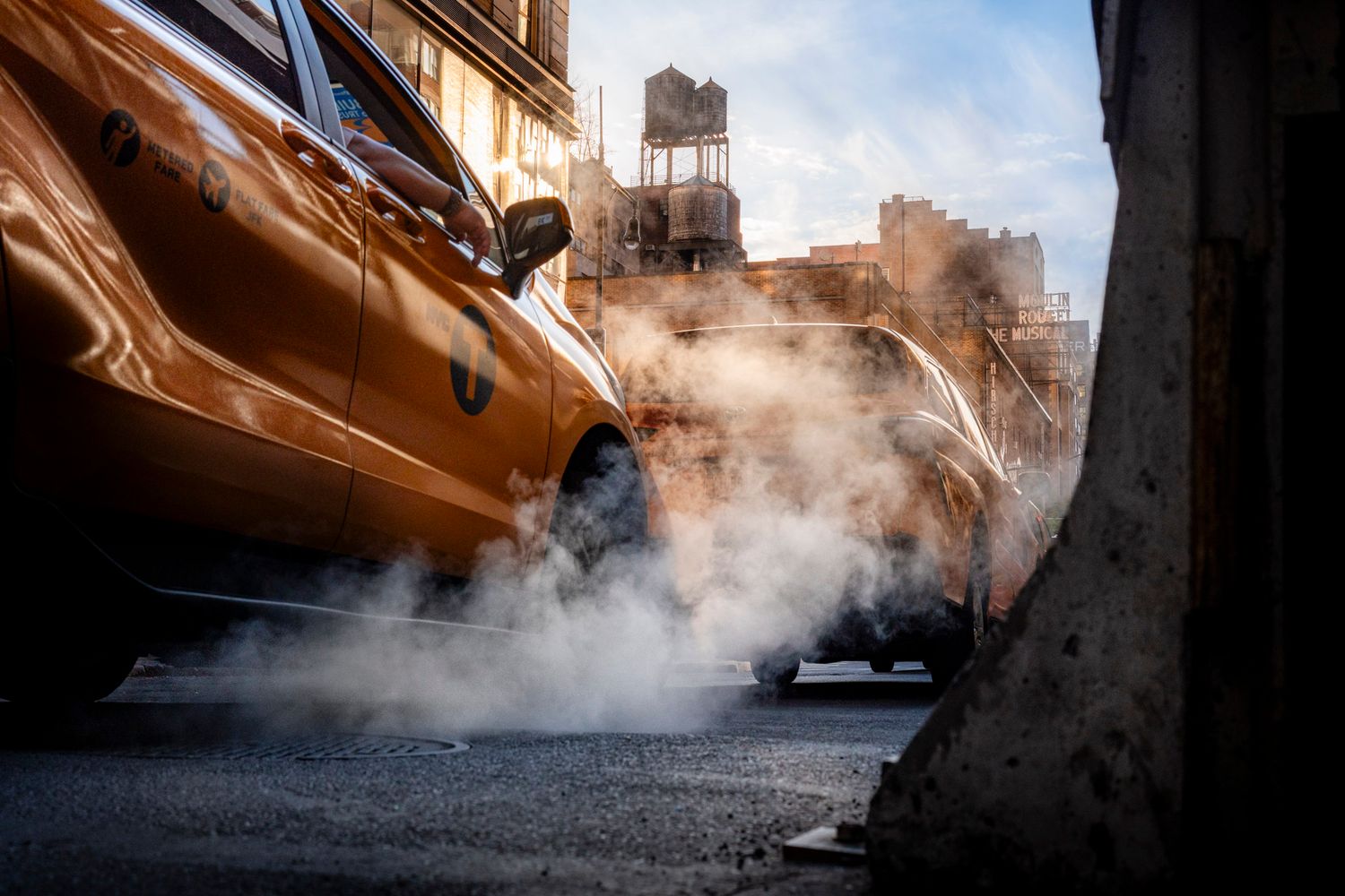 Low-angle view of yellow taxis amid rising steam and New York City water towers