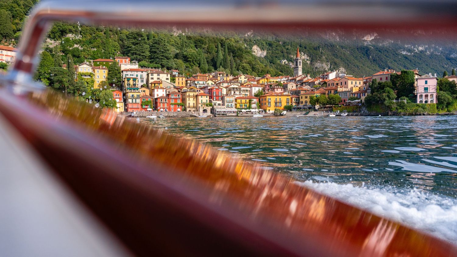 Colorful buildings along the Menaggio waterfront seen through a boat railing on Lake Como.