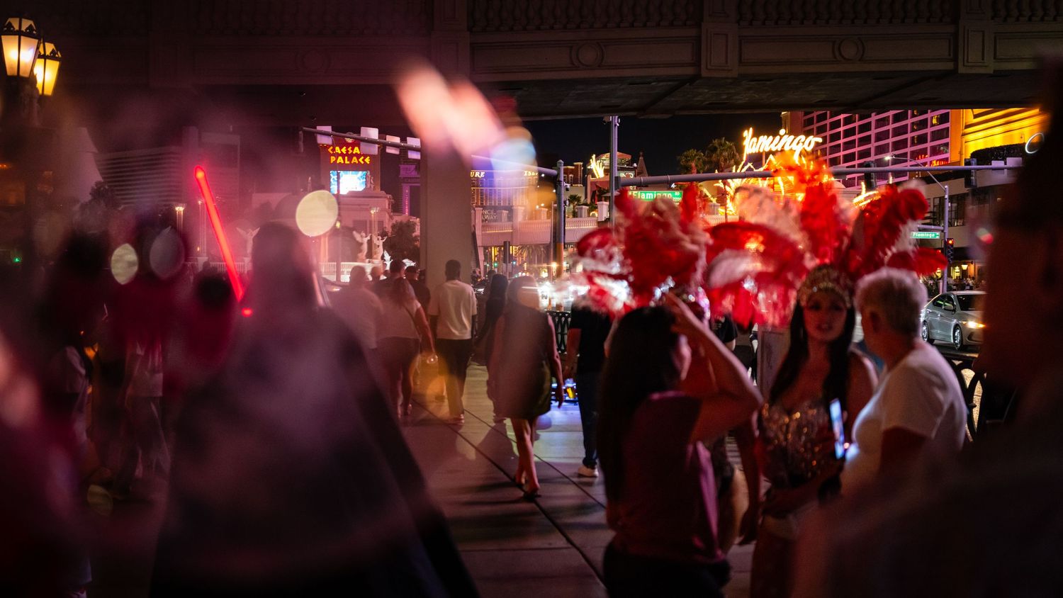 Street performers gathered beneath red neon lights on a crowded Las Vegas sidewalk.