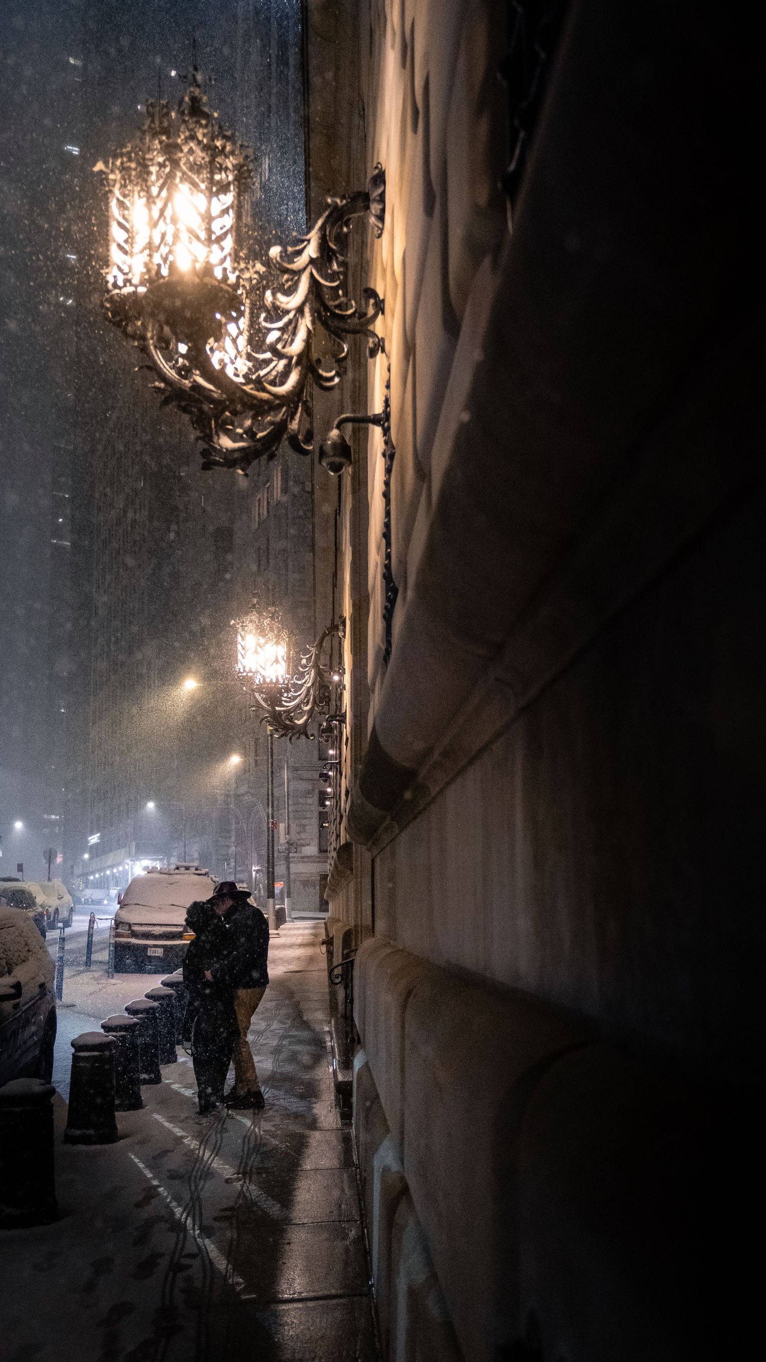 A couple kissing beneath a streetlamp during a snowy night in New York City.
