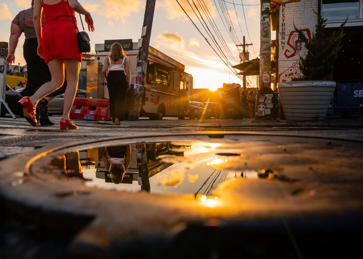Sunlight reflecting in a puddle on a manhole cover as a group of women walk past.