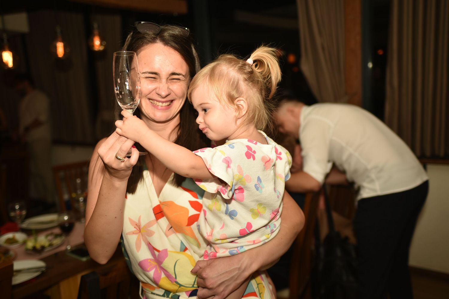 Girl with her mom smiling, reaching out to a glass