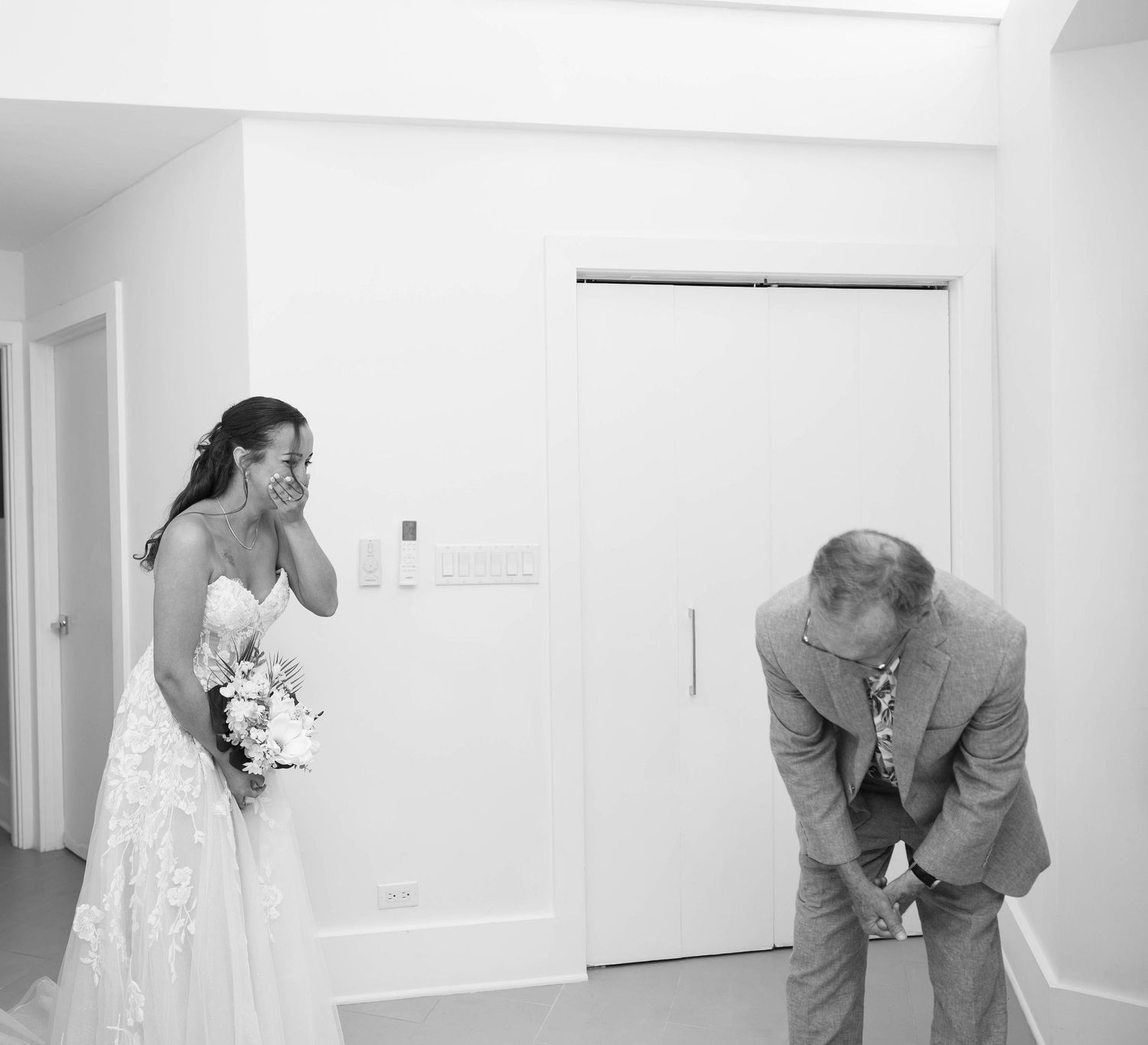 Emotional black and white photo of a bride holding bouquet and father bowing during a wedding first look moment.