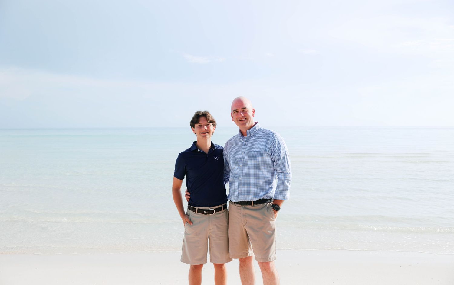 Couple smiling together on a tropical beach with calm turquoise water and clear sky in the background.