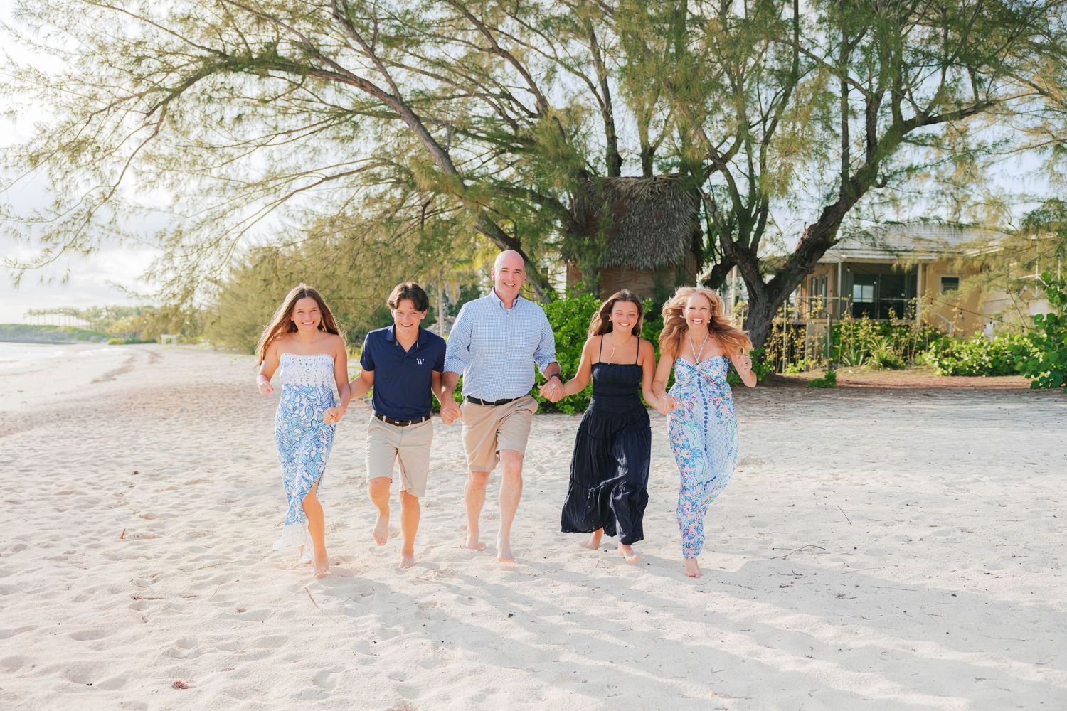 Family of five walking hand-in-hand on a sandy tropical beach, smiling and enjoying a sunny day outdoors.