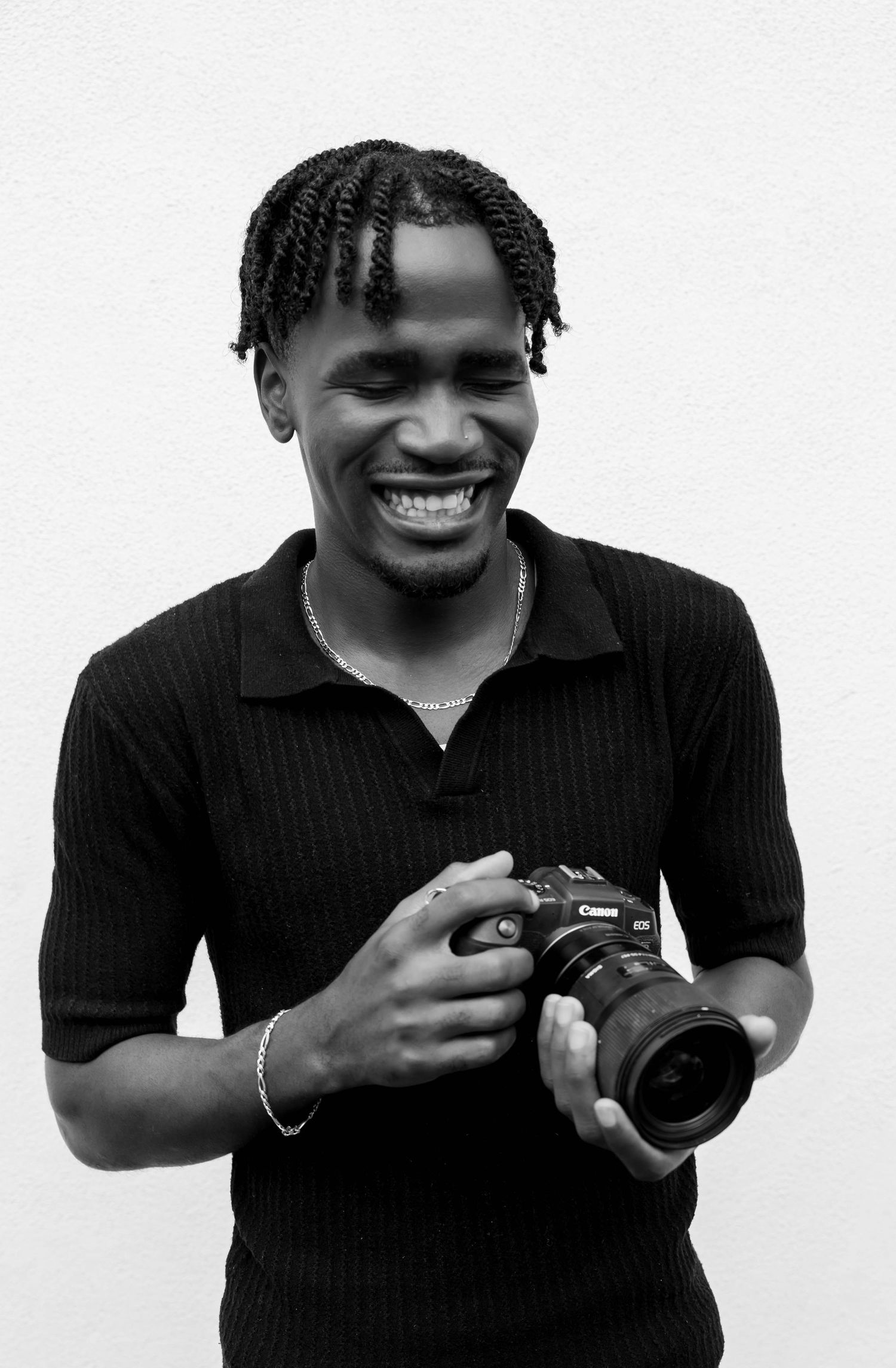 Smiling young Black male photographer holding a Canon camera in a black and white portrait photo.