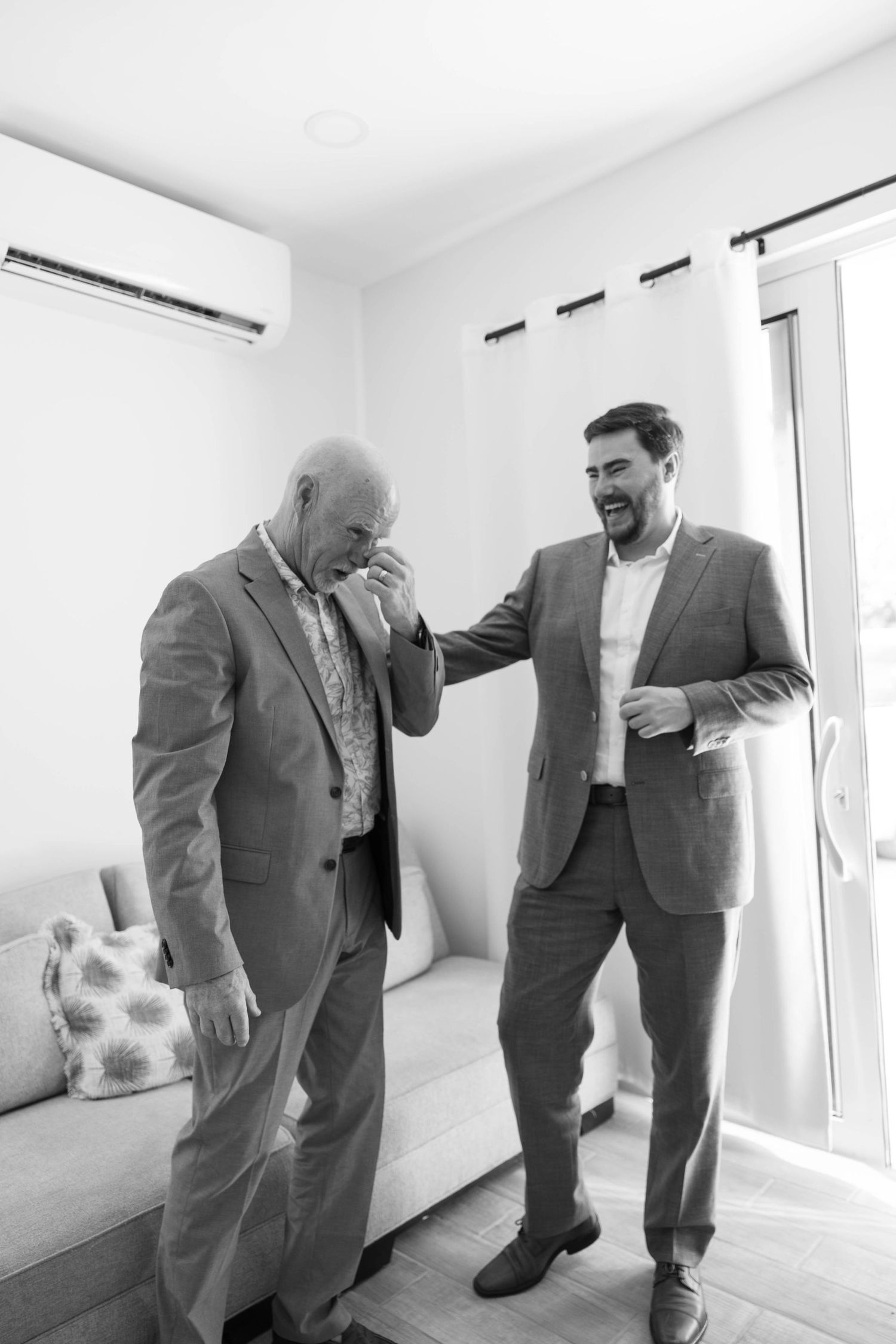 Black and white photo of a groom and his emotional father sharing a heartfelt moment before the wedding.