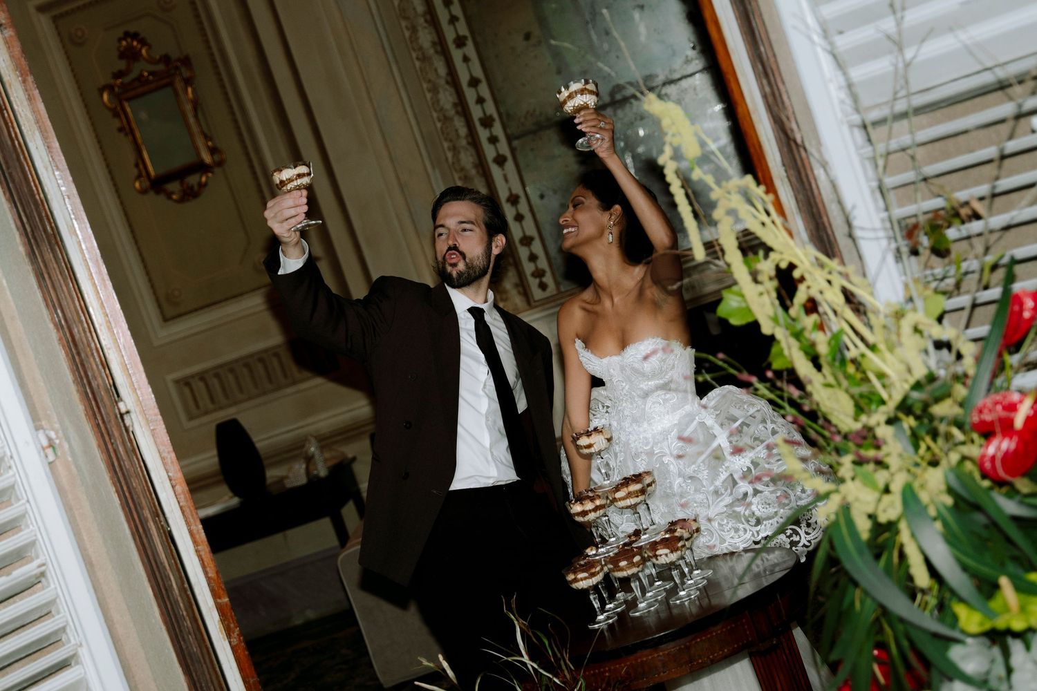 Bride and groom raising champagne glasses in elegant venue during wedding toast celebration.