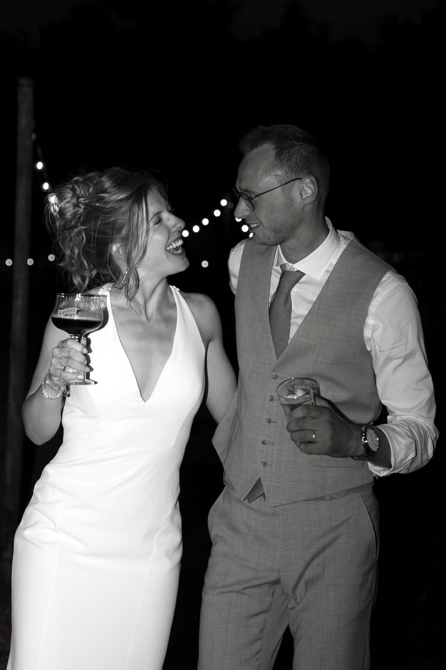 Black and white photo of a smiling bride and groom holding drinks at their wedding reception.