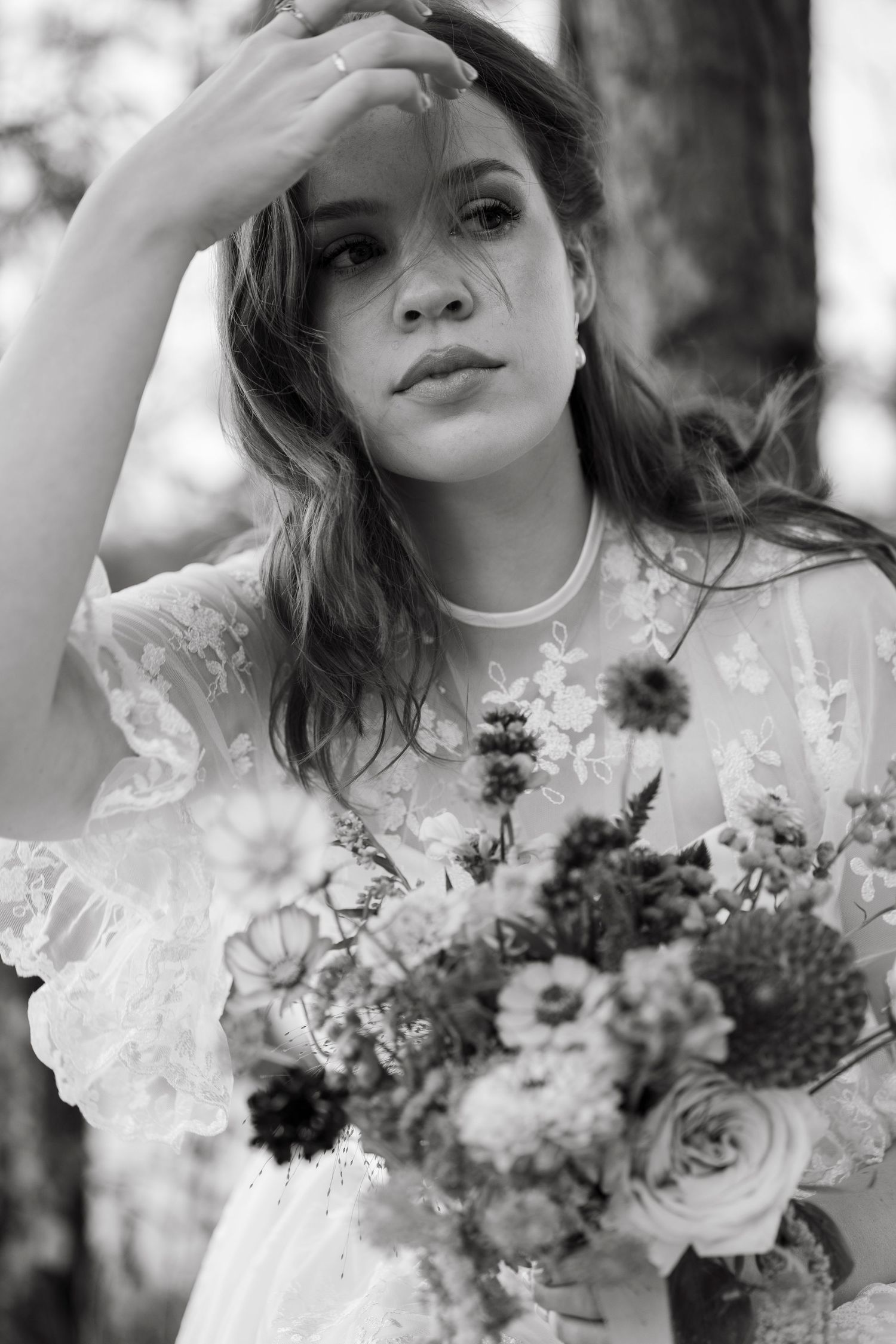Black and white portrait of a bride holding a floral bouquet, wearing a lace dress outdoors.