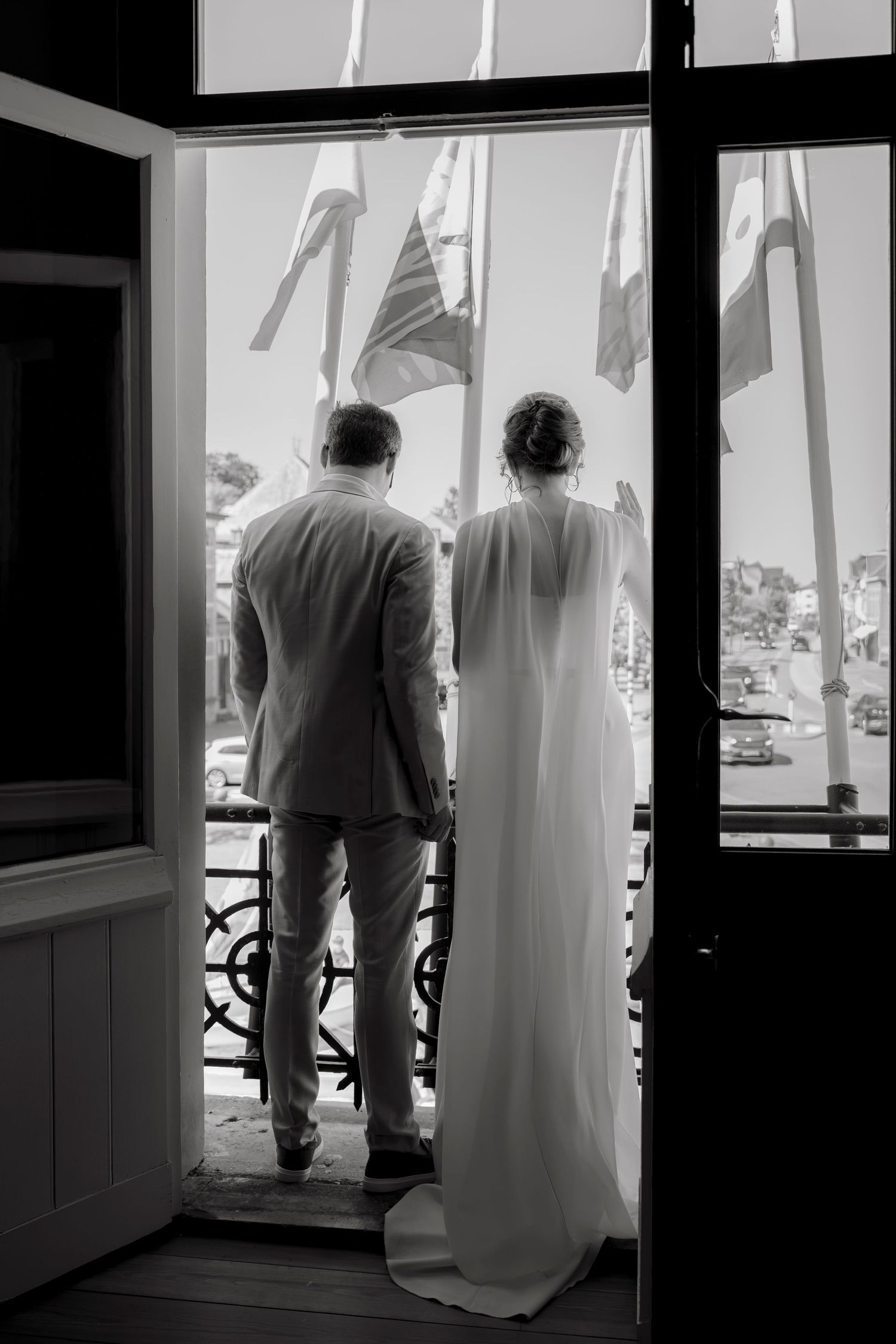 Black and white photo of bride and groom standing in doorway looking out at flags and scenic view on their wedding day.
