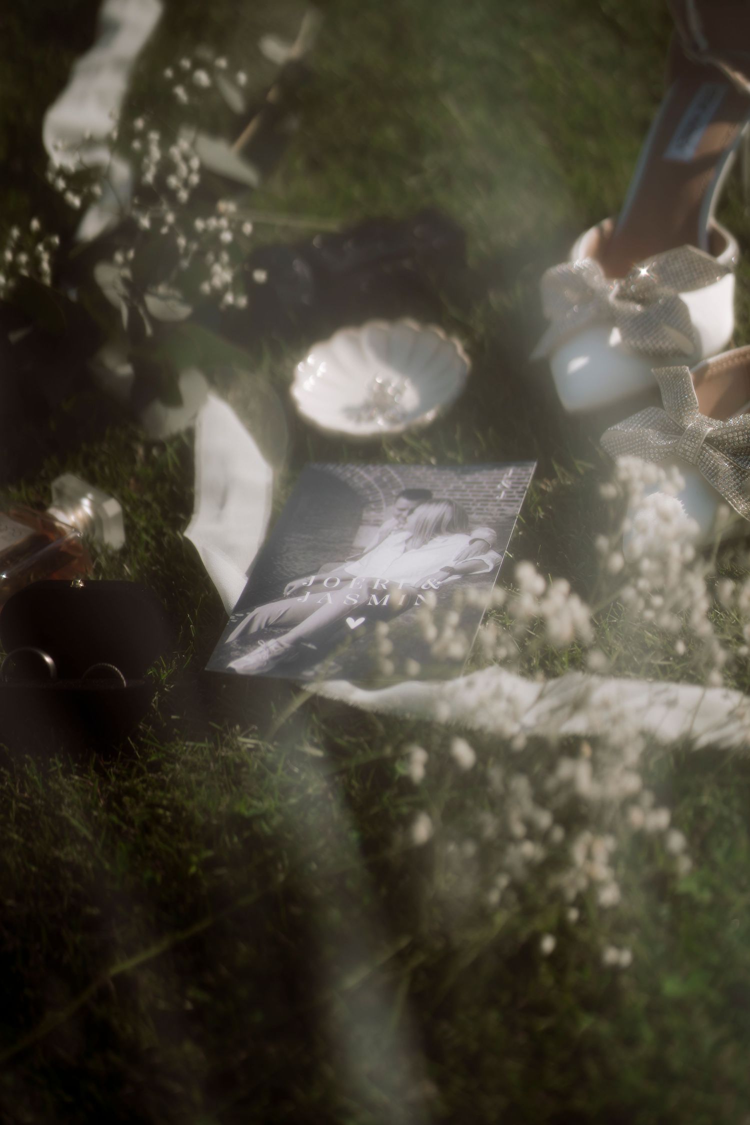 Dreamy flat lay on grass with a photo, white flowers, candles, and soft bokeh light creating an ethereal mood.
