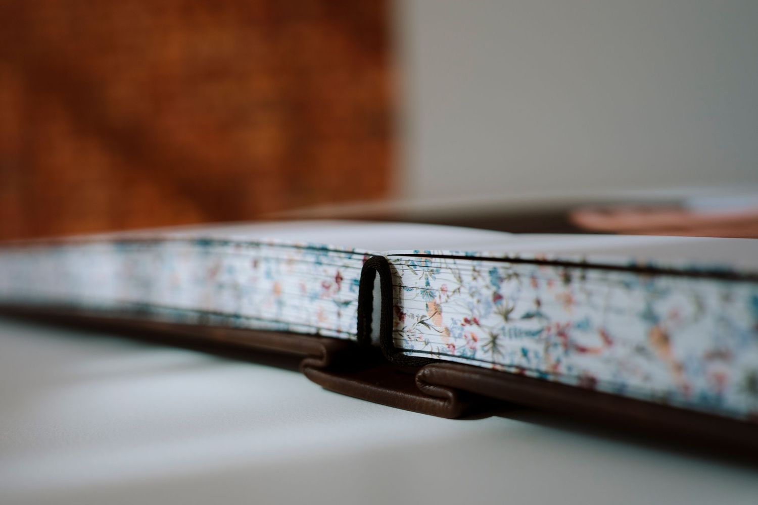 Close-up of a decorative hardcover book spine with floral pattern and metal clasp on white surface.