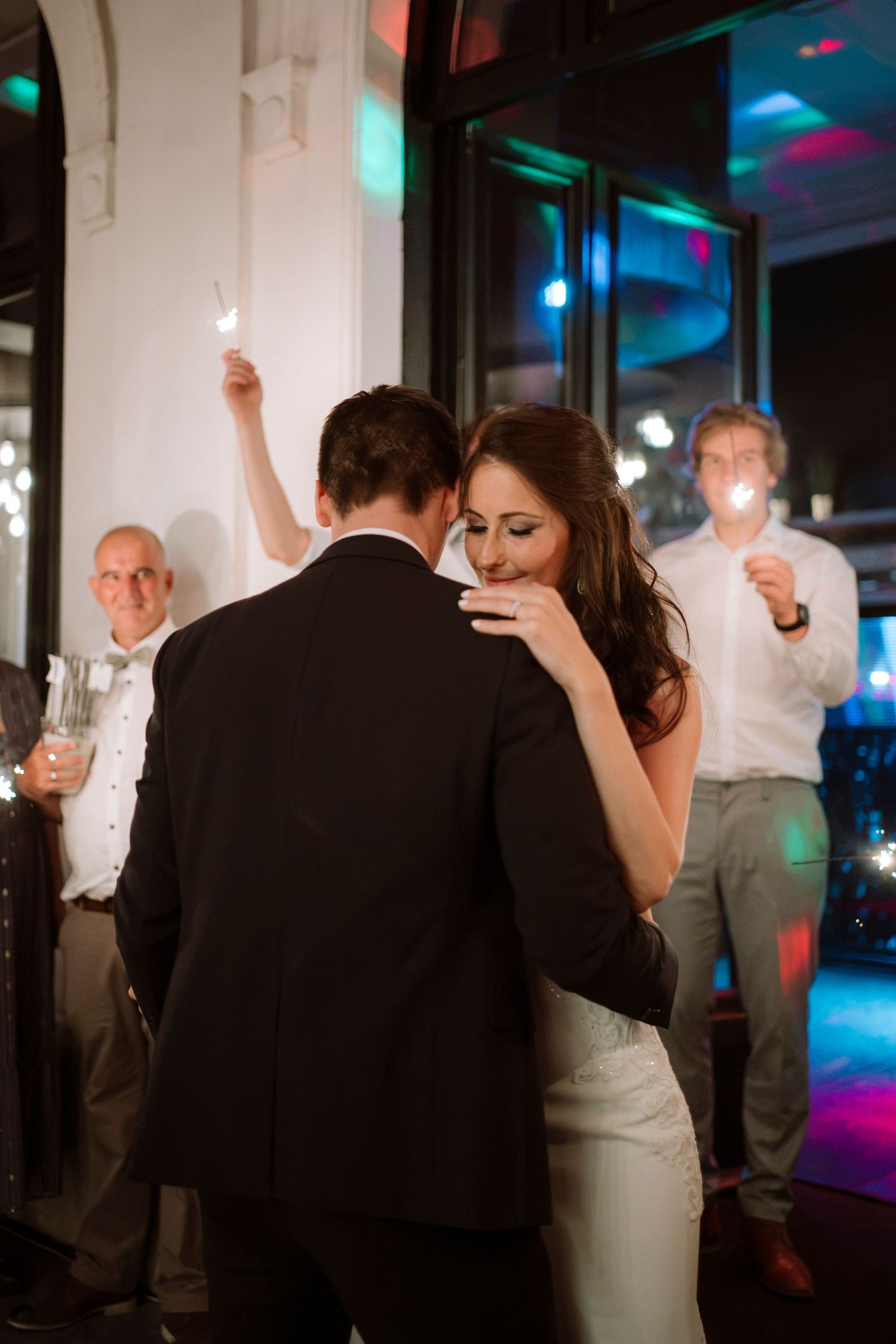 Bride and groom share first dance while guests hold sparklers at elegant evening wedding reception.