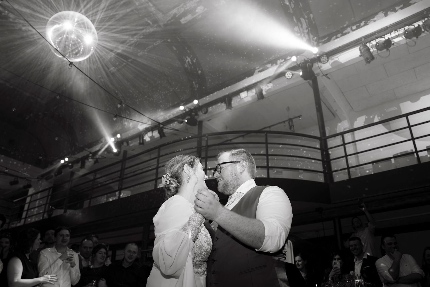 Couple shares first dance under disco ball at wedding reception in black and white photo.