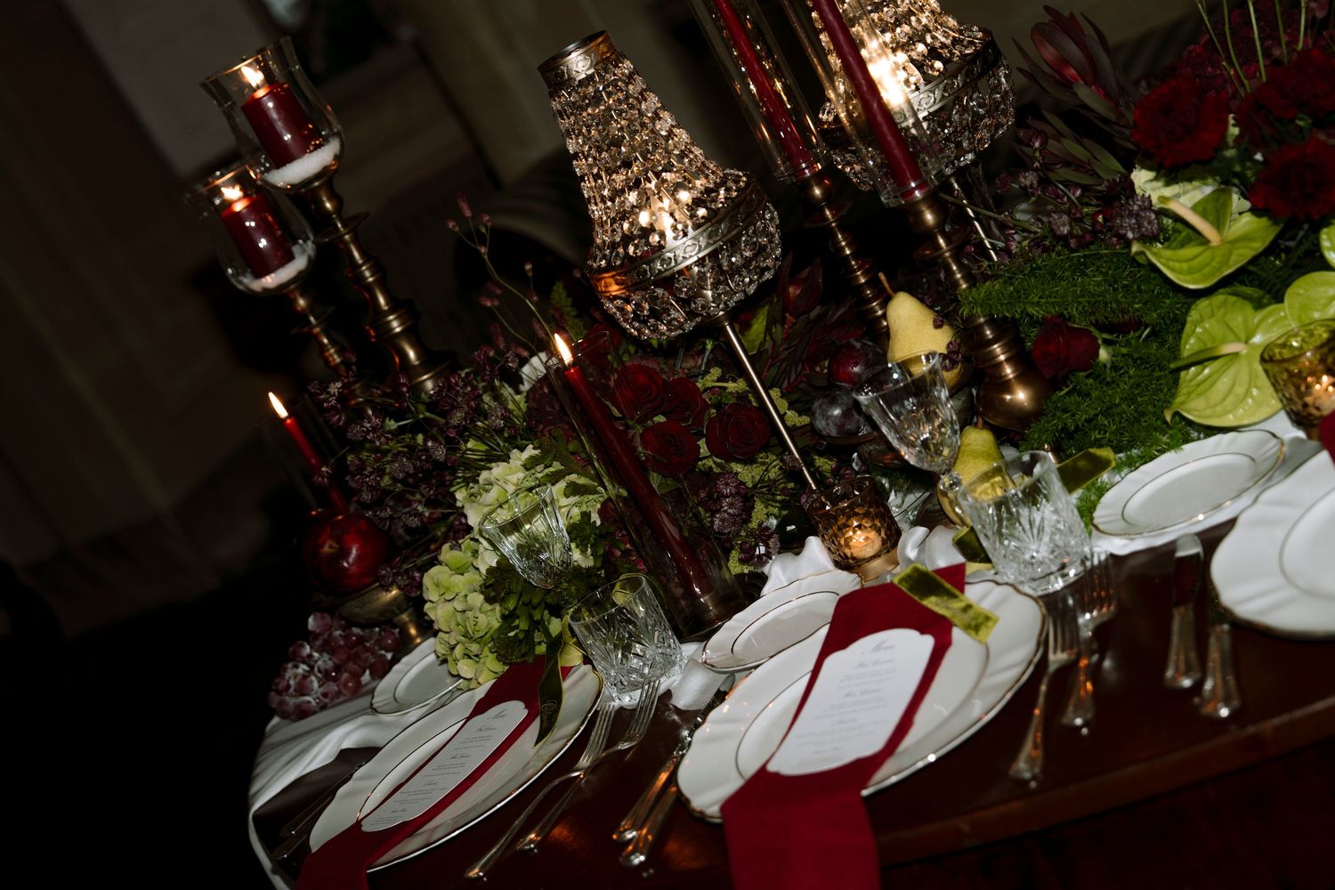 Elegant formal dining table set with red napkins, crystal candelabras, white plates, and lush floral centerpieces.