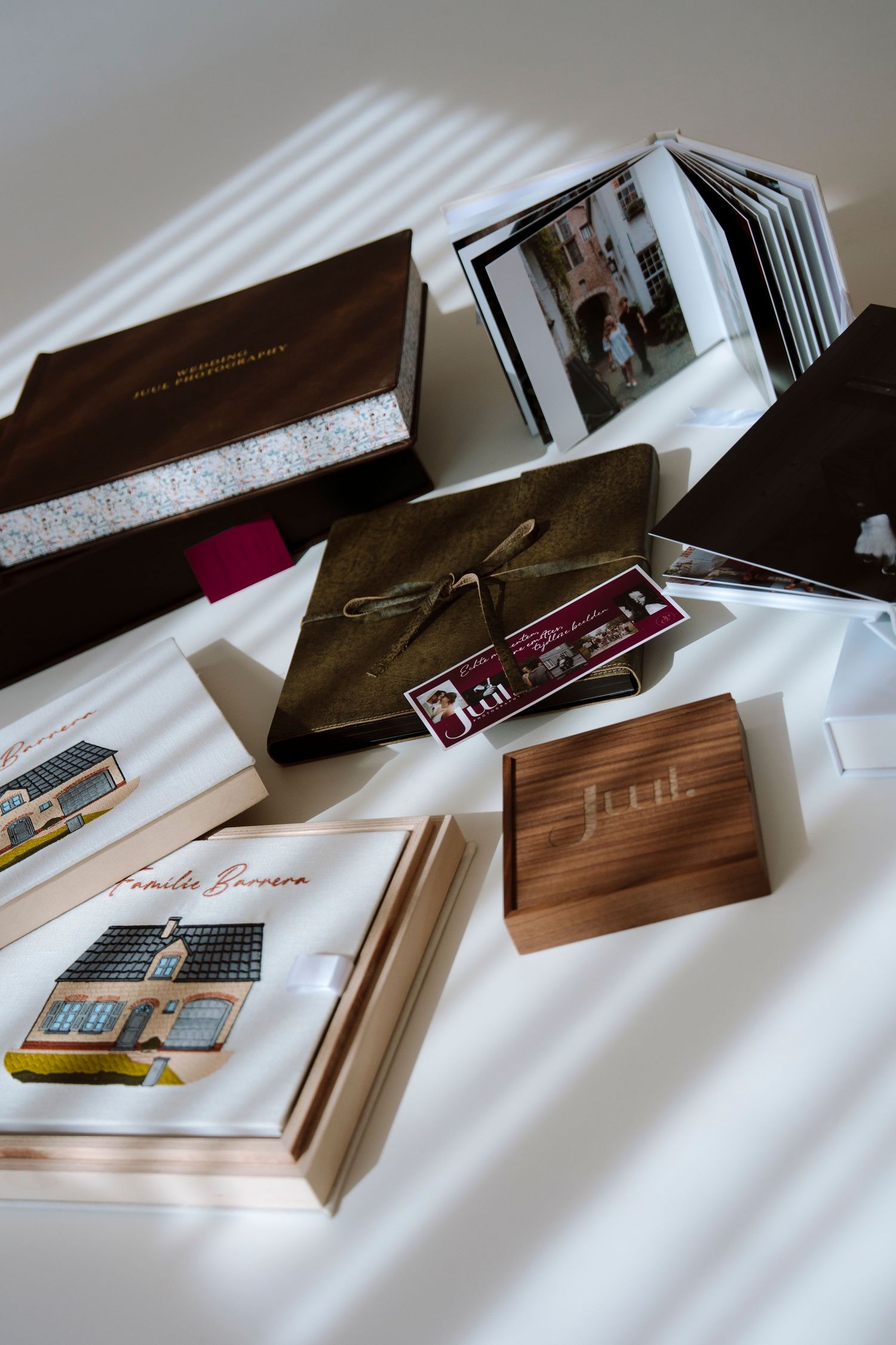 Assorted photo albums, wooden boxes, and keepsake books arranged on a white surface with natural light shadows.
