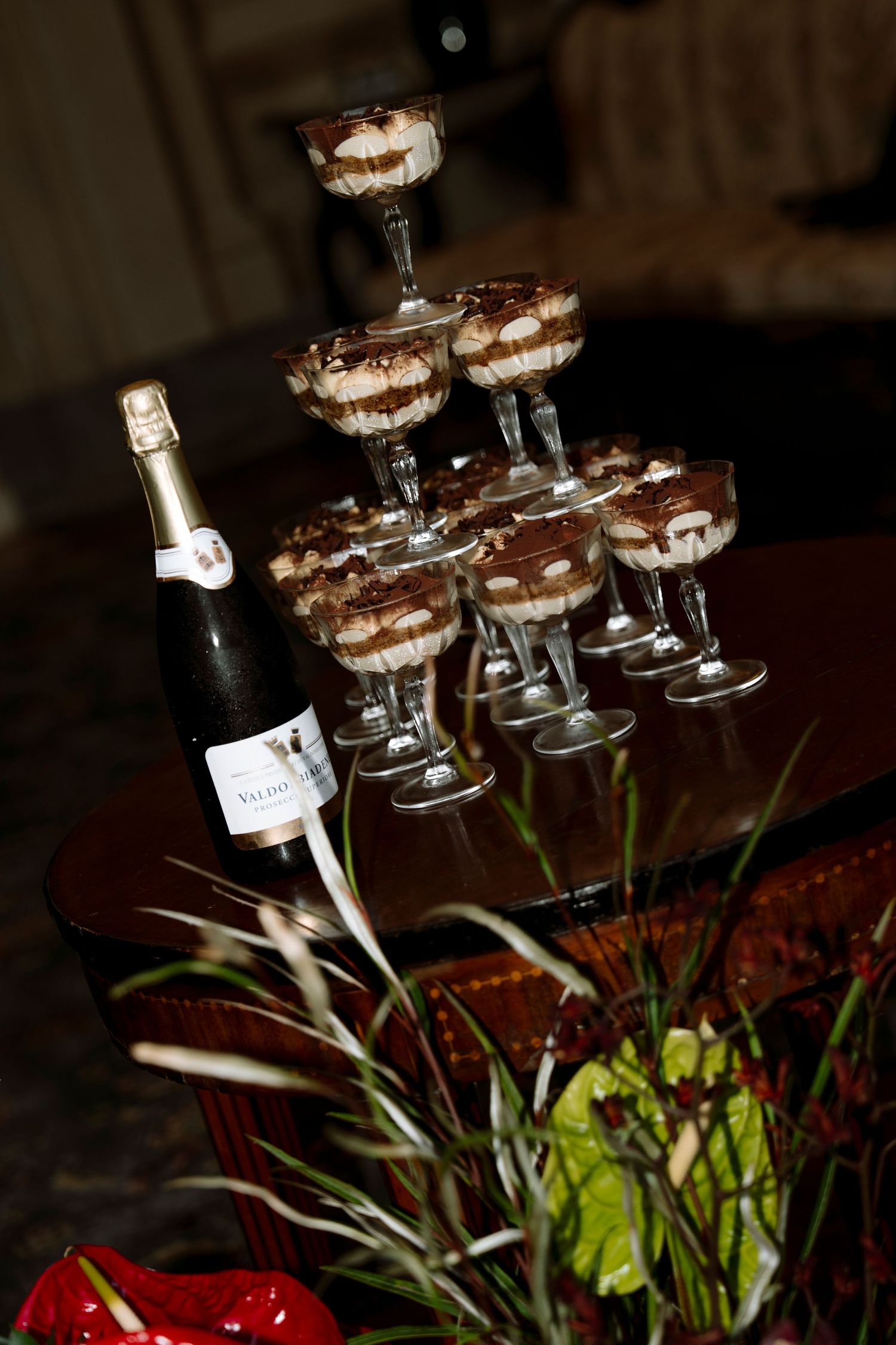 Elegant tiramisu desserts served in champagne glasses stacked in a pyramid next to a bottle of sparkling wine.