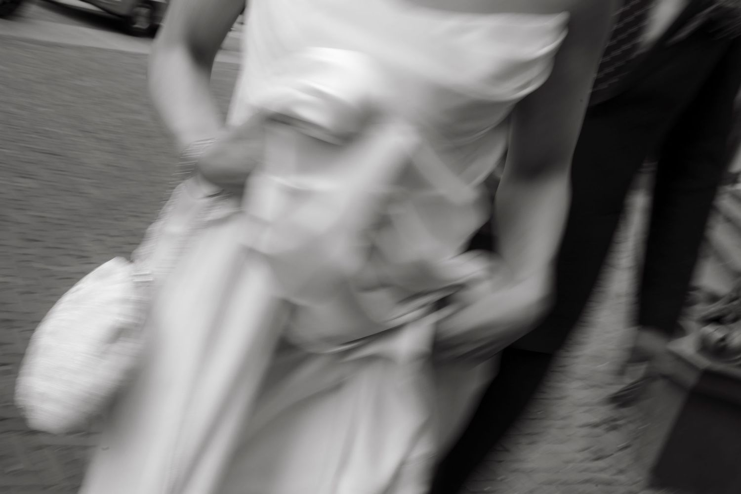 Blurred black and white photo of a woman in a white wedding dress, captured in motion outdoors.