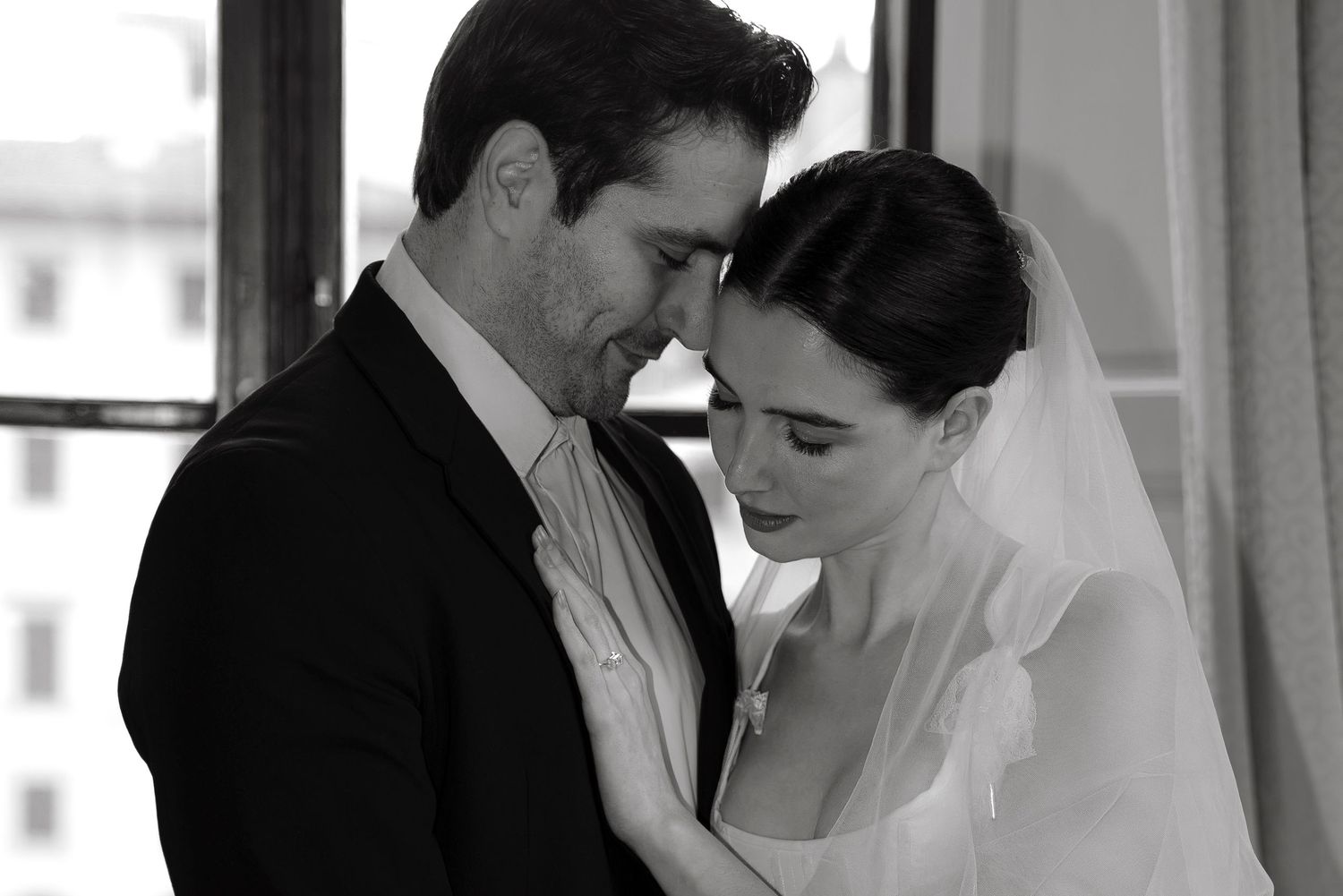 Black and white wedding photo of bride and groom sharing an intimate moment, touching foreheads tenderly.