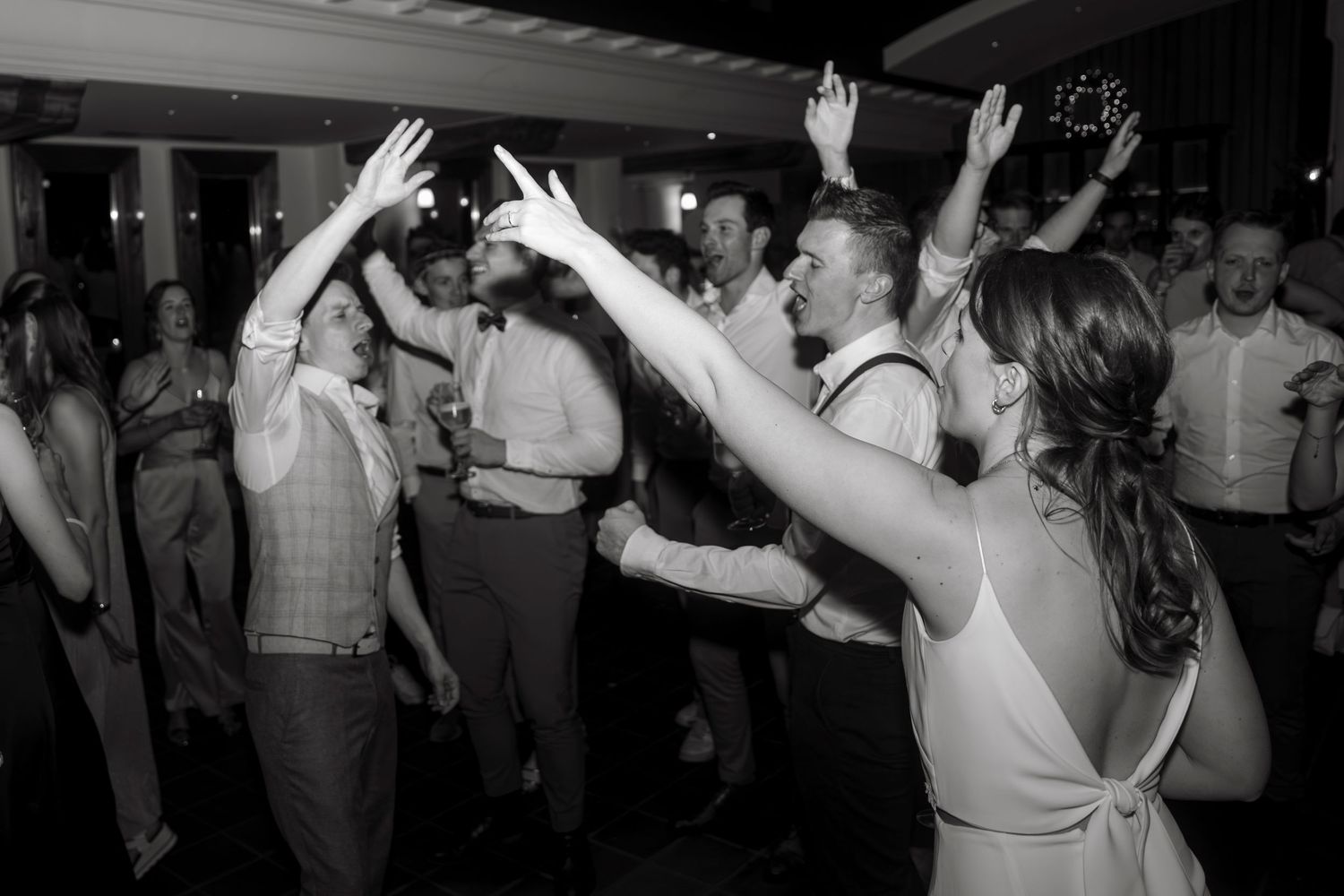 Black and white photo of wedding guests dancing with arms raised at a lively wedding reception party.