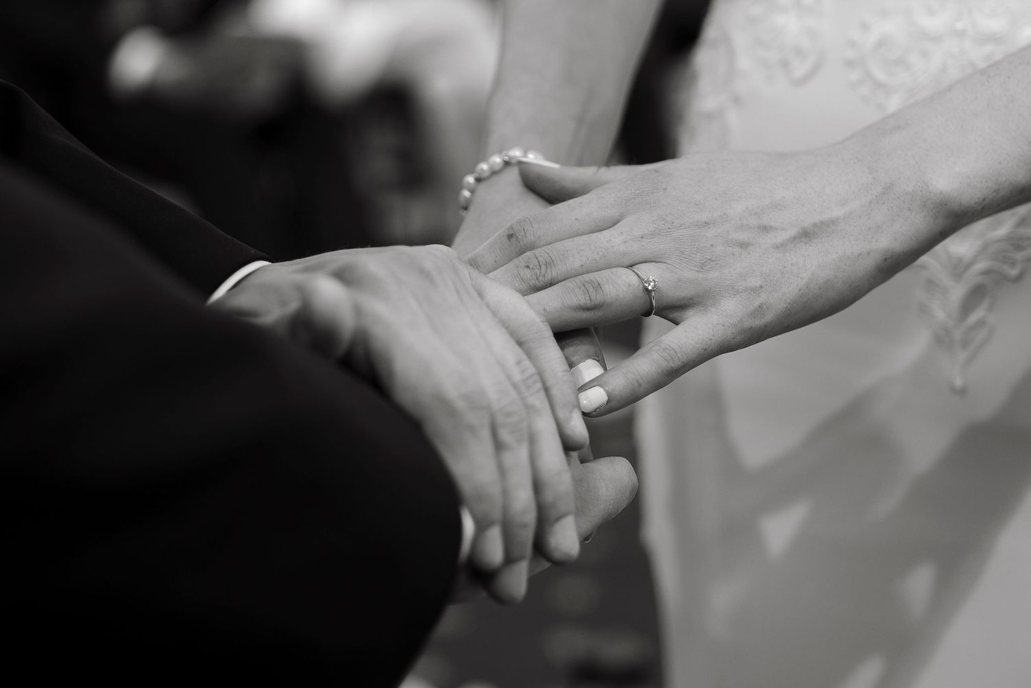 Black and white photo of bride and groom exchanging wedding rings during marriage ceremony.