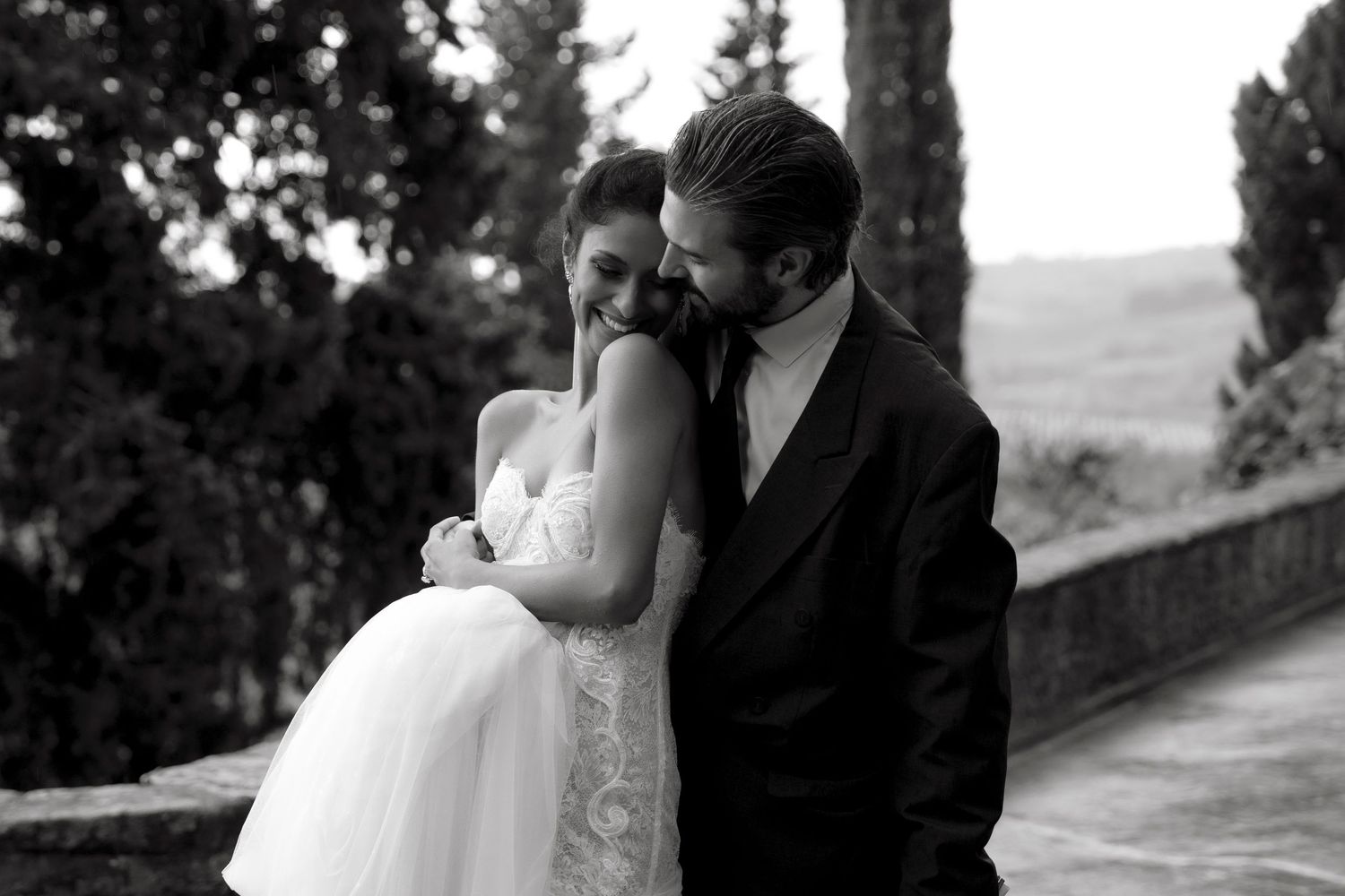 Black and white photo of a bride and groom sharing a tender moment, smiling together outdoors.