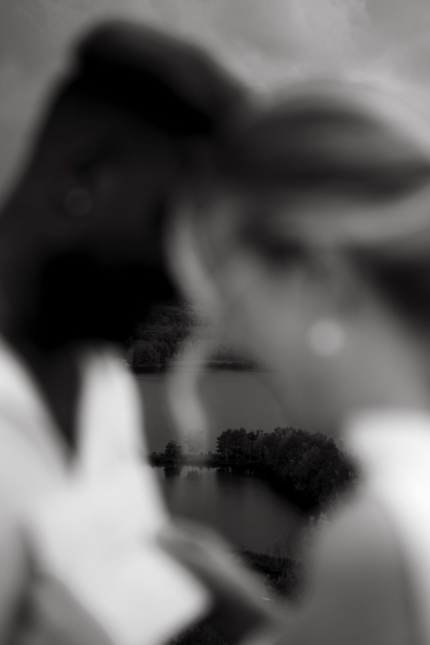 Black and white double exposure of two people with a serene lake and trees reflected between them.