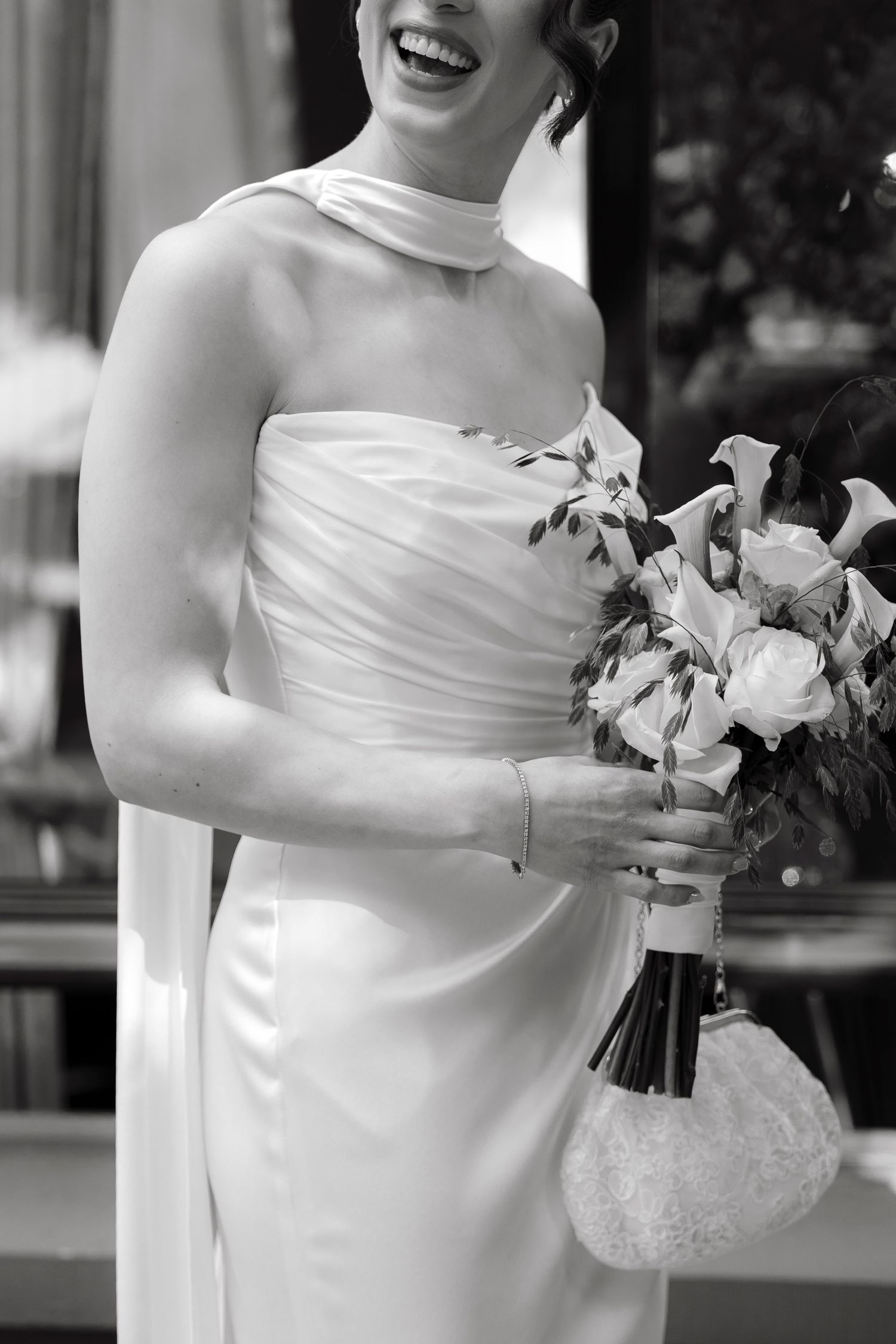 Black and white photo of a smiling bride in a white gown holding a bouquet of calla lilies on her wedding day.