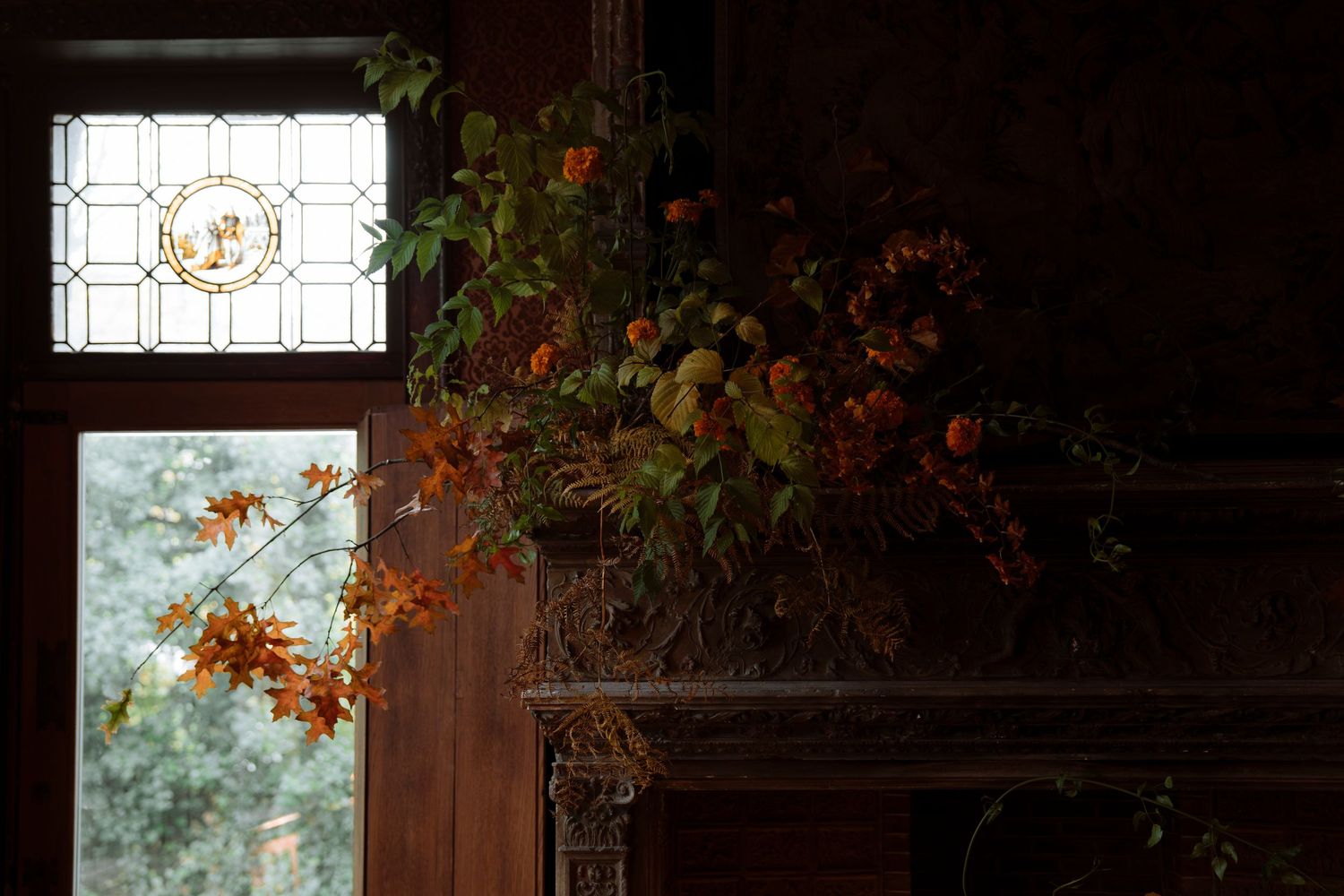 Autumn floral arrangement with orange blooms near stained glass window in dark wood interior.
