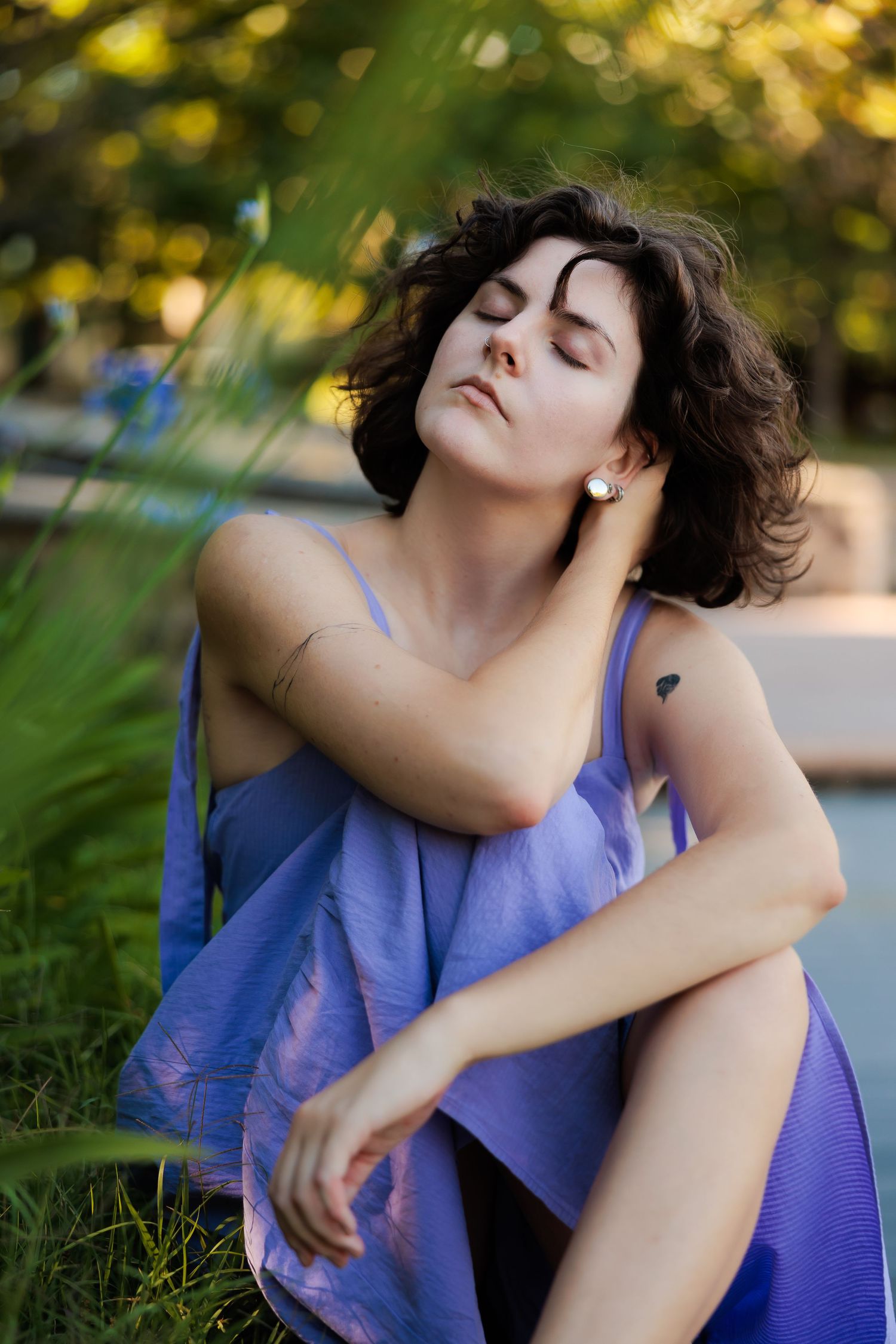 Woman in purple dress lying on grass during golden hour with dreamy expression.